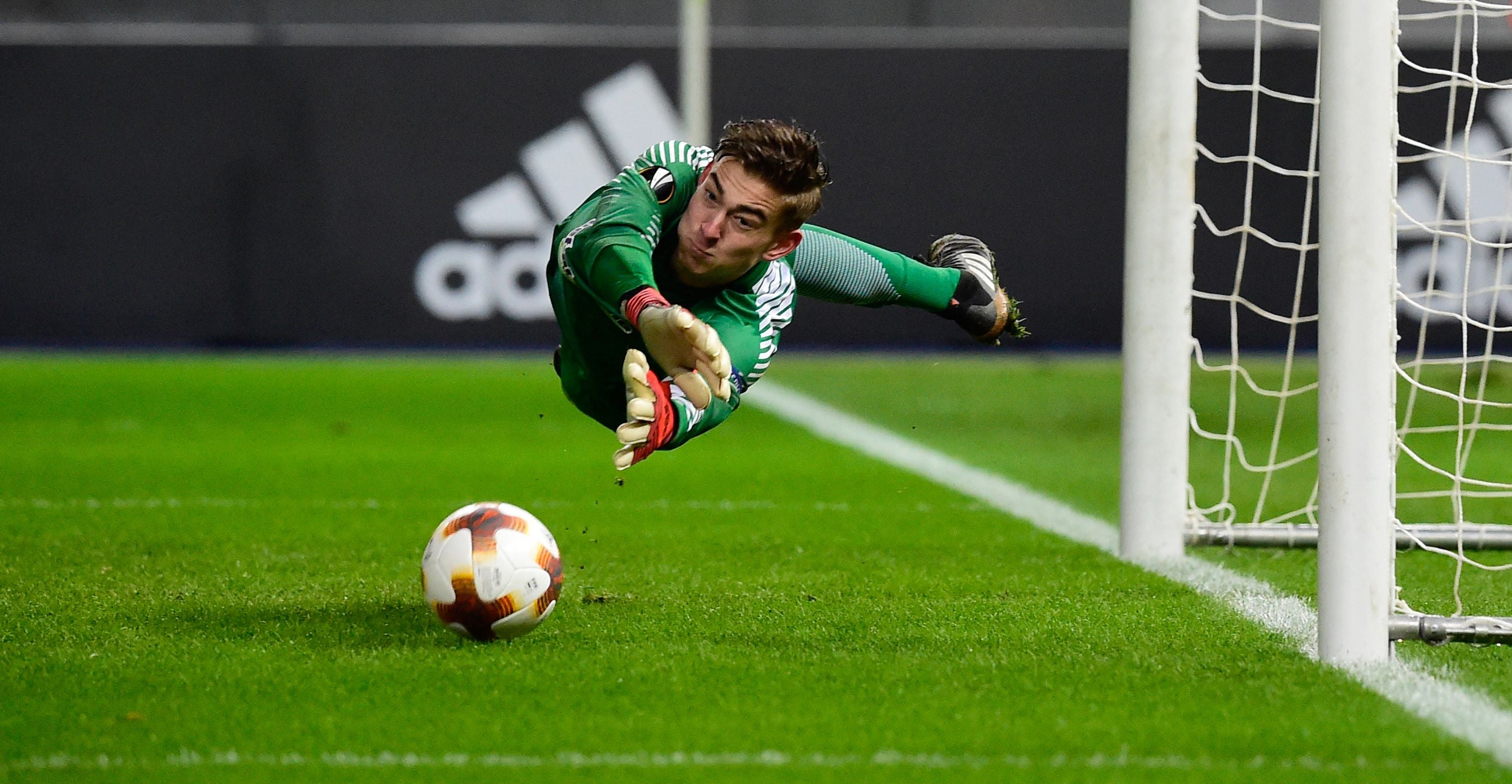 Torwart in grüner Kleidung hechtet, um einen Fußball vor dem Tor zu halten.