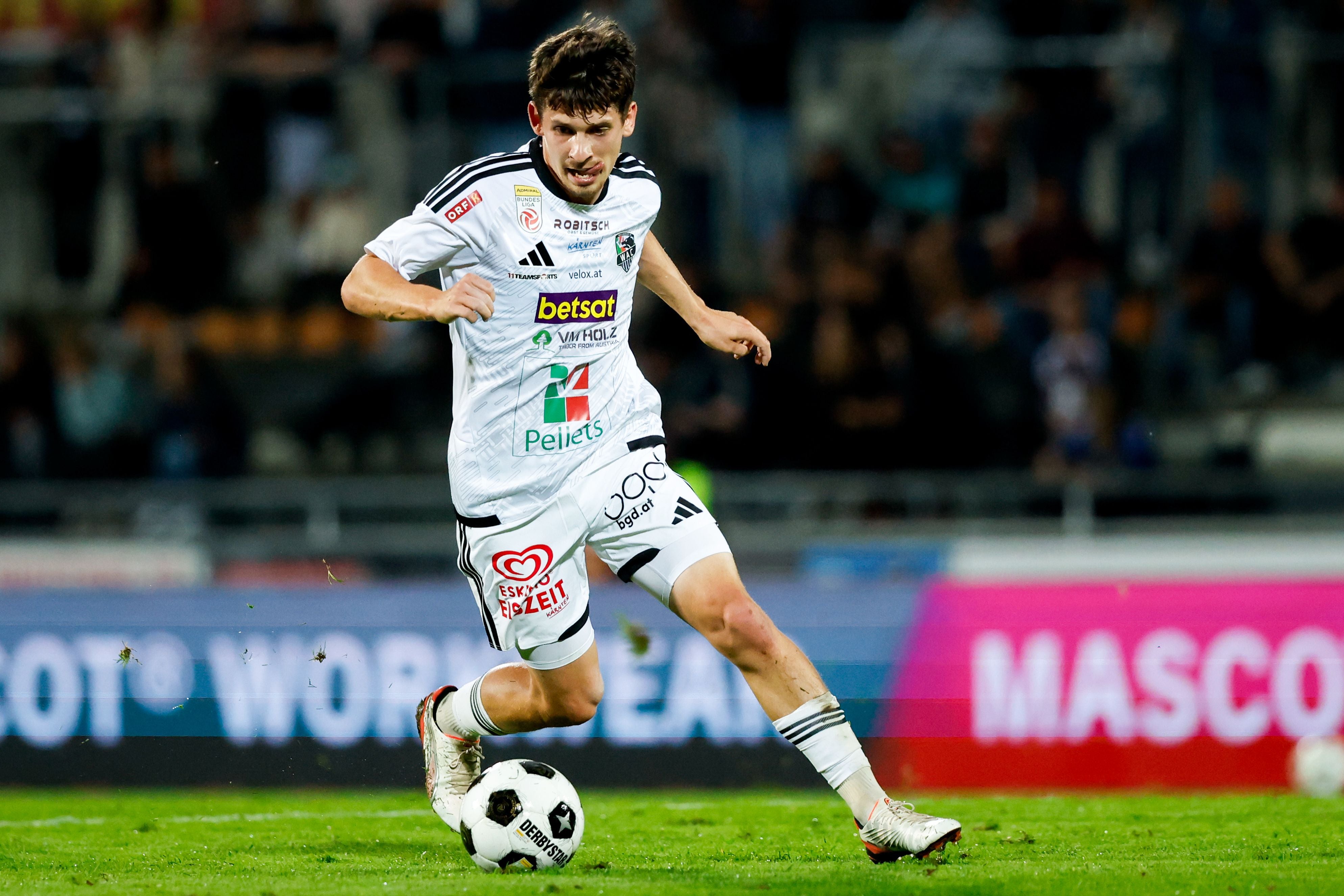 Ein Fußballspieler im weißen Trikot läuft mit dem Ball über das Spielfeld.