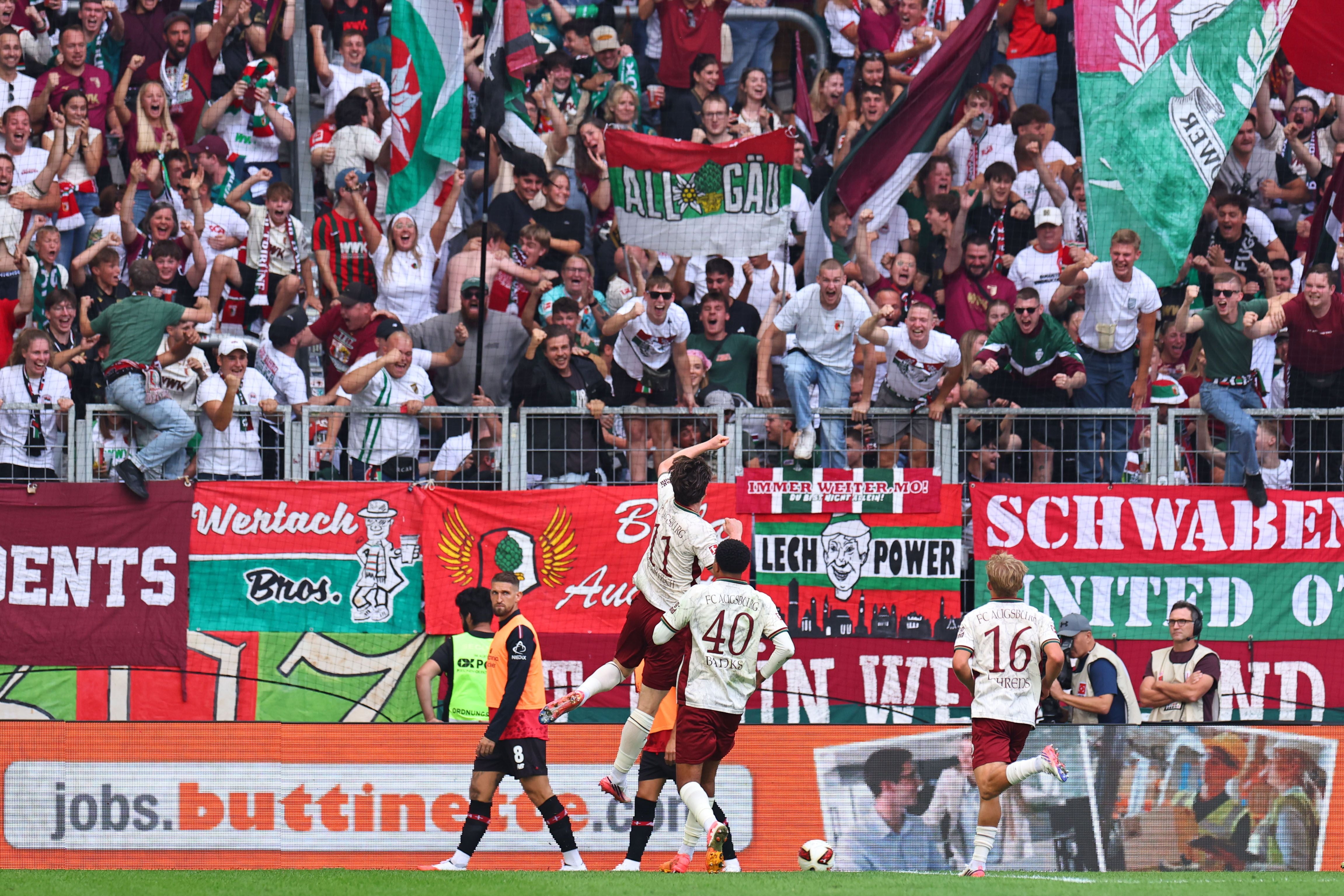 Fußballspieler von Augsburg jubeln mit Fans nach einem Tor gegen Leverkusen im Stadion.