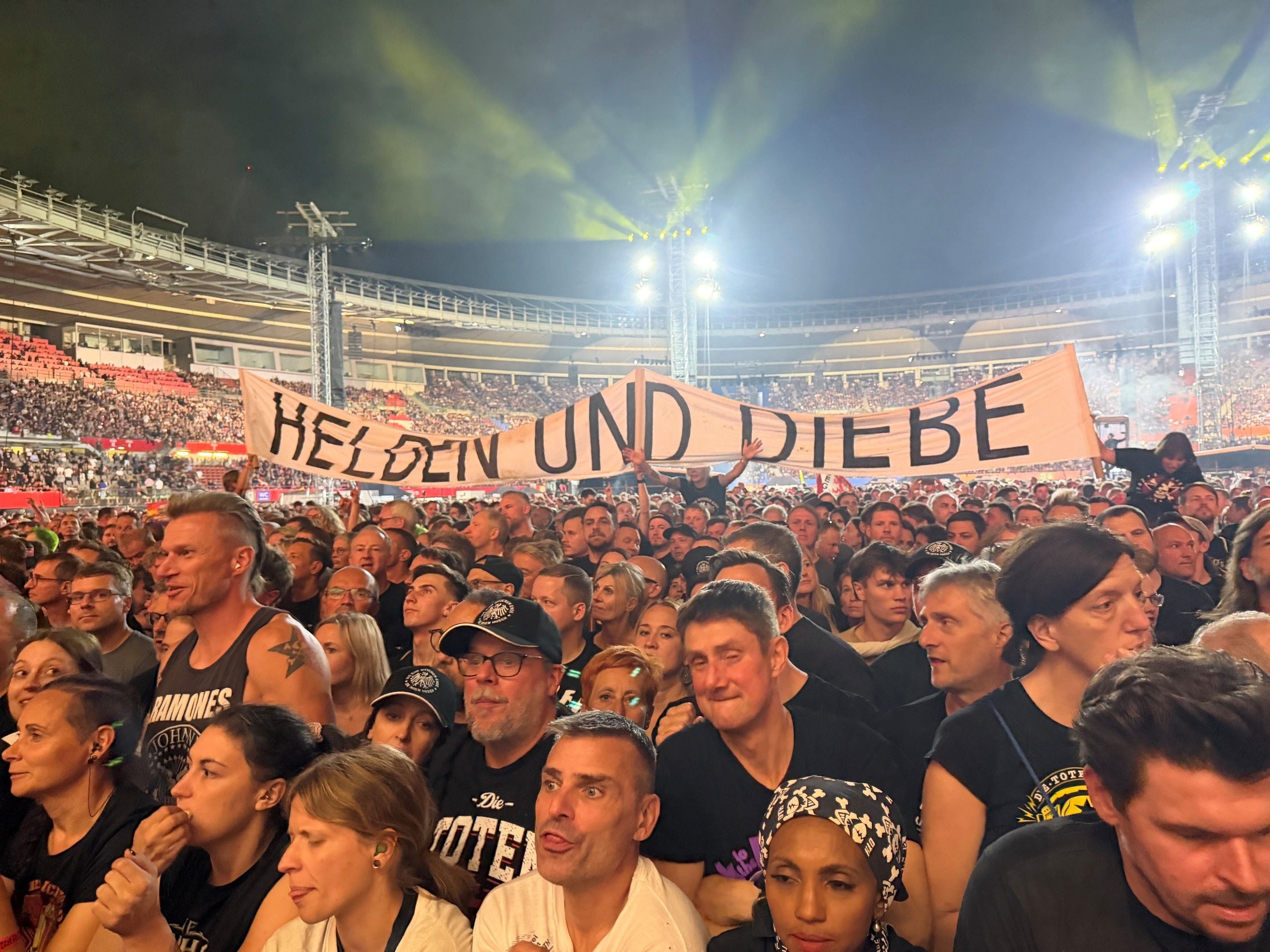 Menschenmenge bei einem Die Toten Hosen-Konzert, Banner mit „Helden und Diebe“ im Hintergrund.