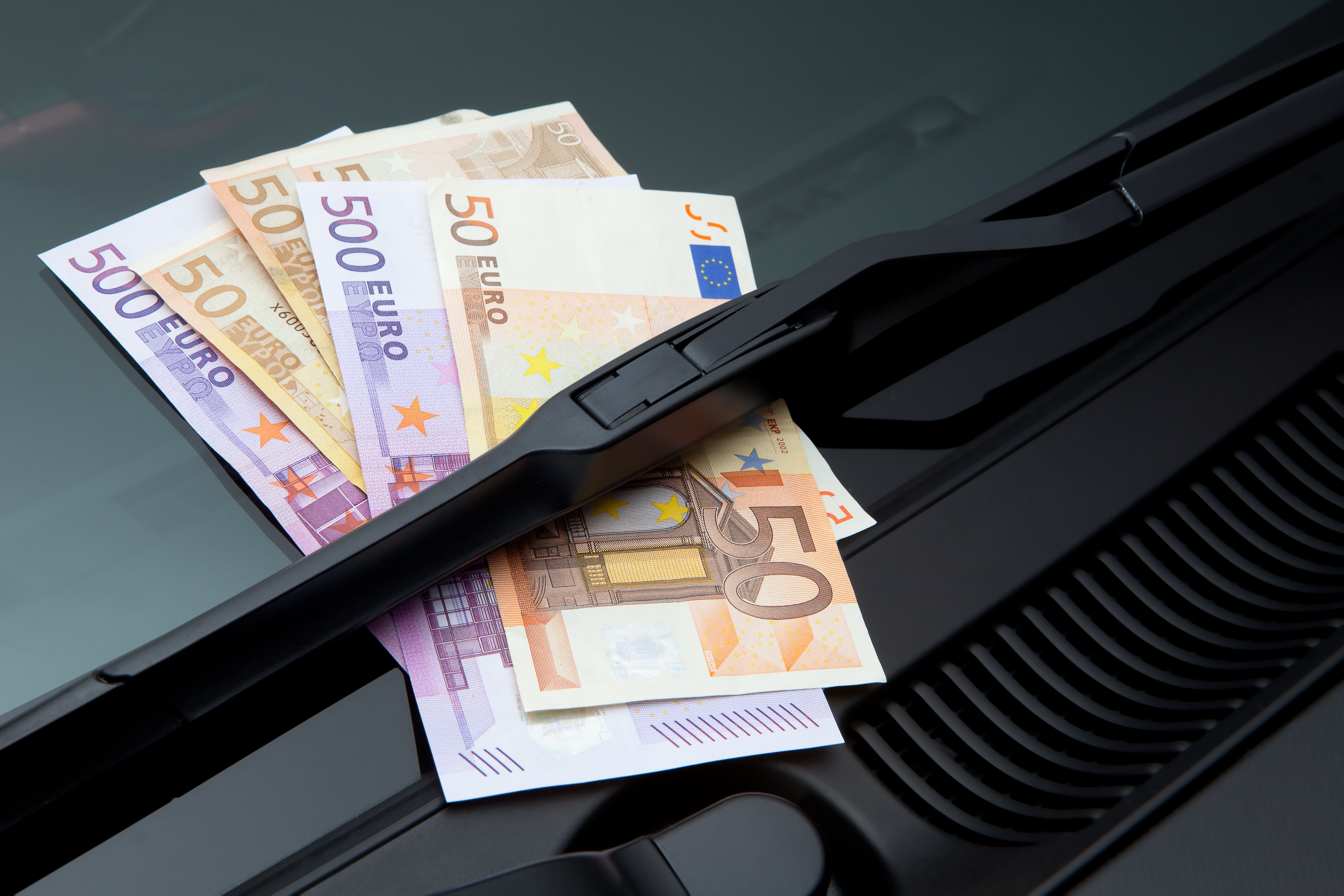 Mehrere Euro-Geldscheine stecken unter einem Scheibenwischer auf einer Windschutzscheibe.