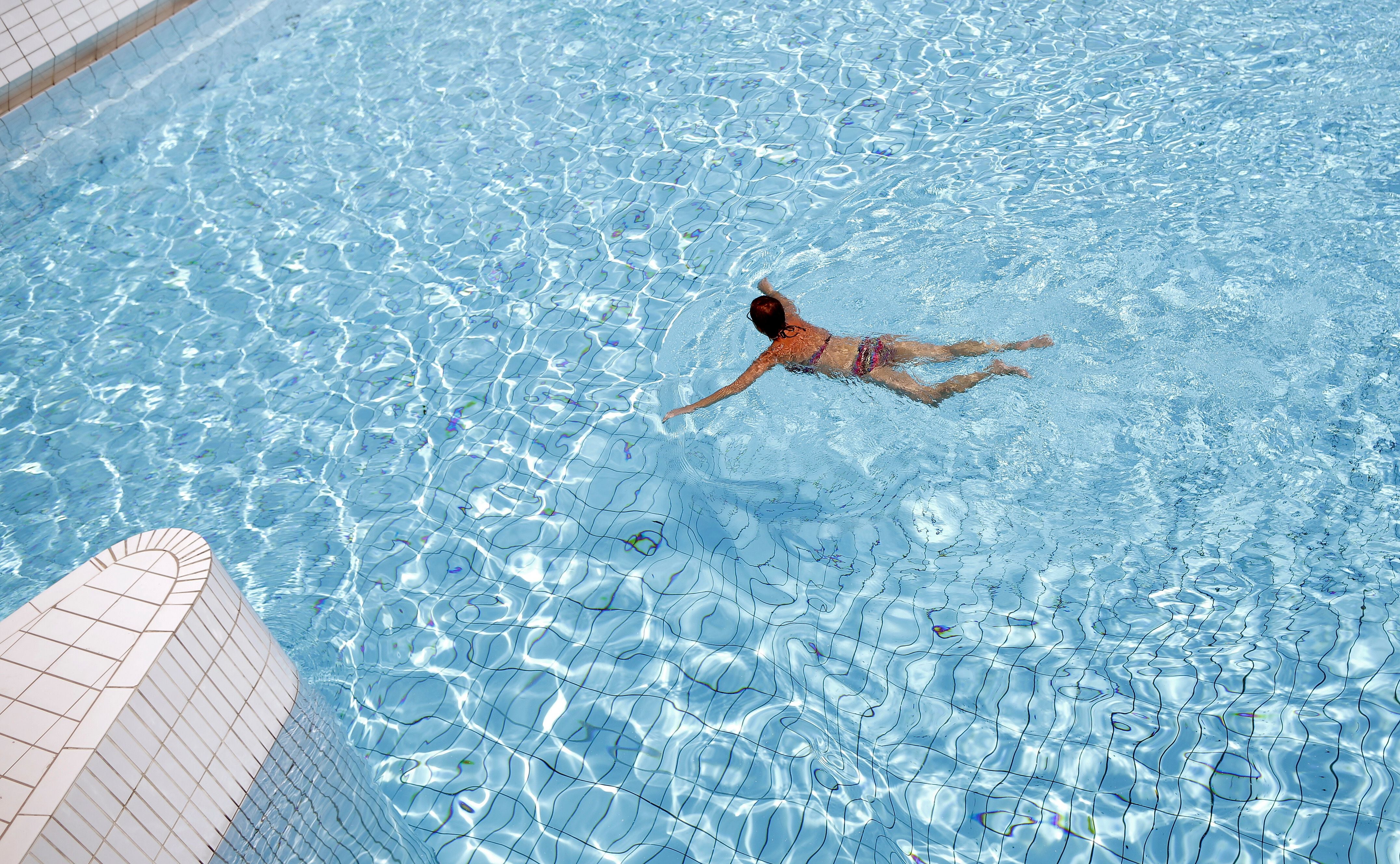 Eine Frau schwimmt allein in einem klaren Schwimmbecken bei sonnigem Wetter.