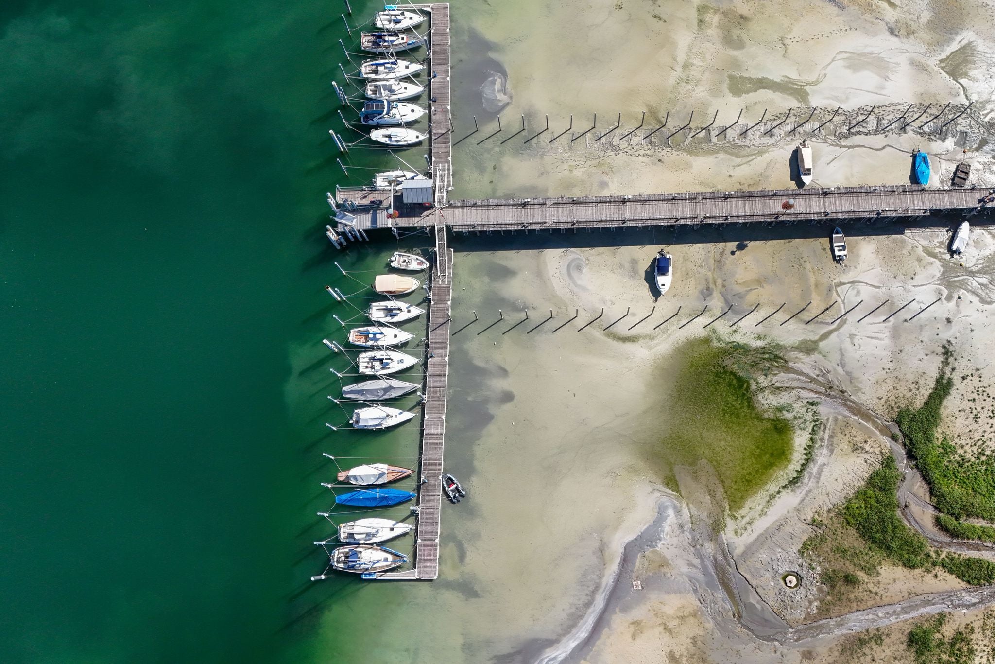 Luftaufnahme eines Stegs am Bodensee, mehrere Boote liegen im flachen Wasser und teils auf dem Trockenen.