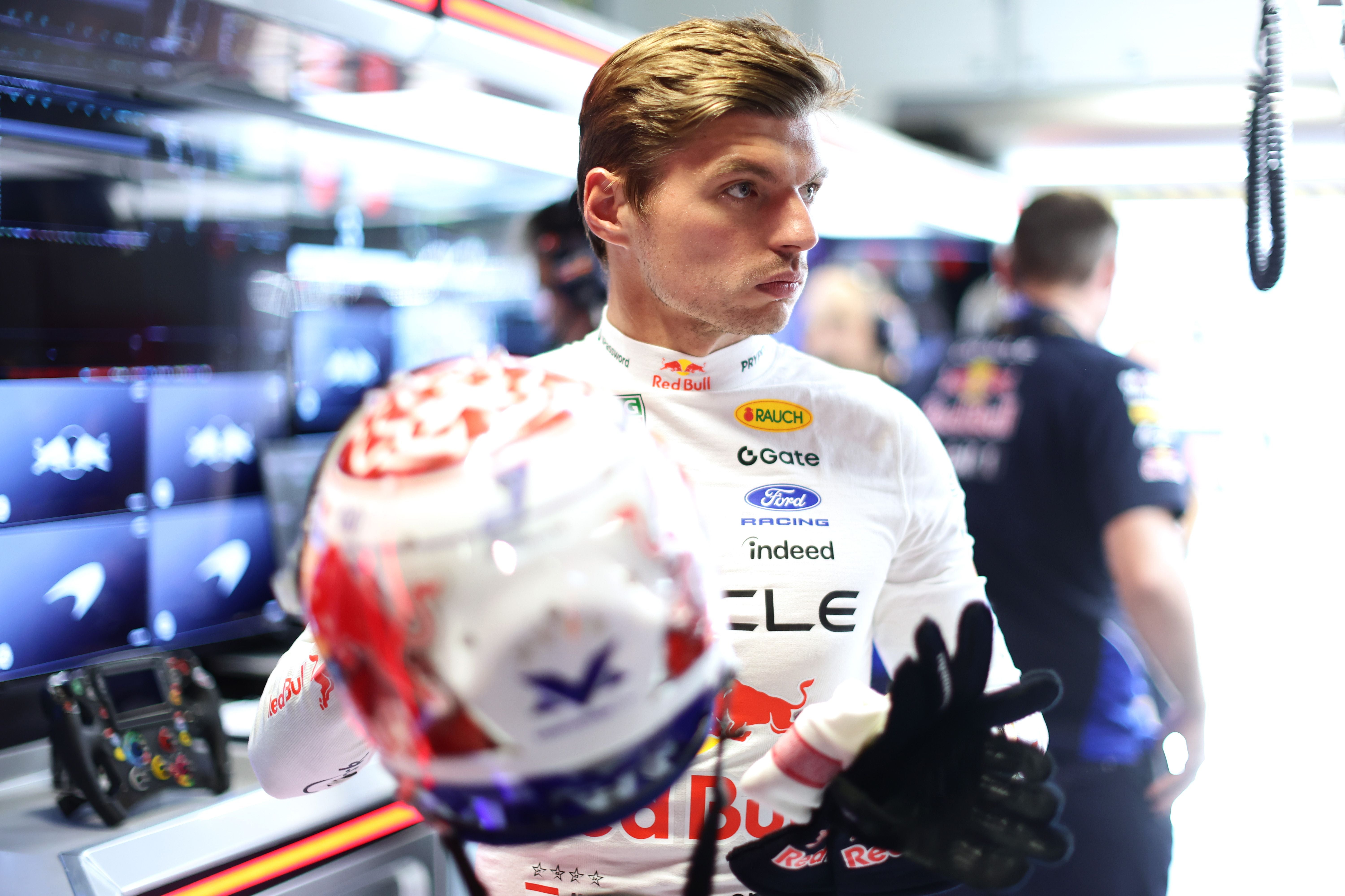 Ein Rennfahrer im weißen Red-Bull-Anzug steht in einer Formel-1-Garage und hält seinen Helm.