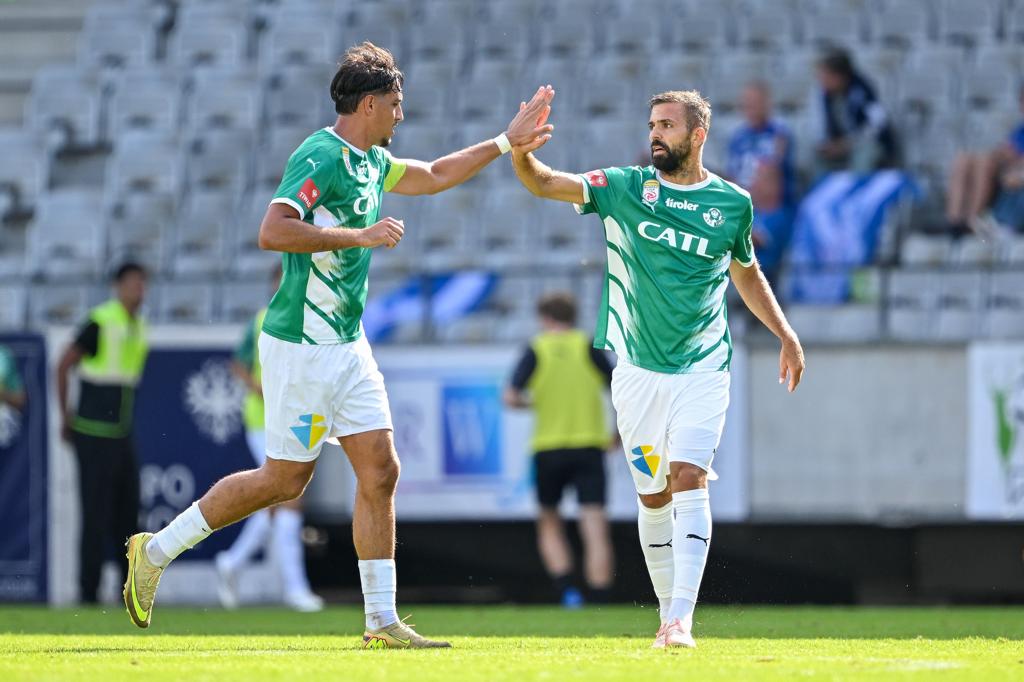 Zwei Fußballspieler im grünen Trikot klatschen sich während eines Spiels ab.