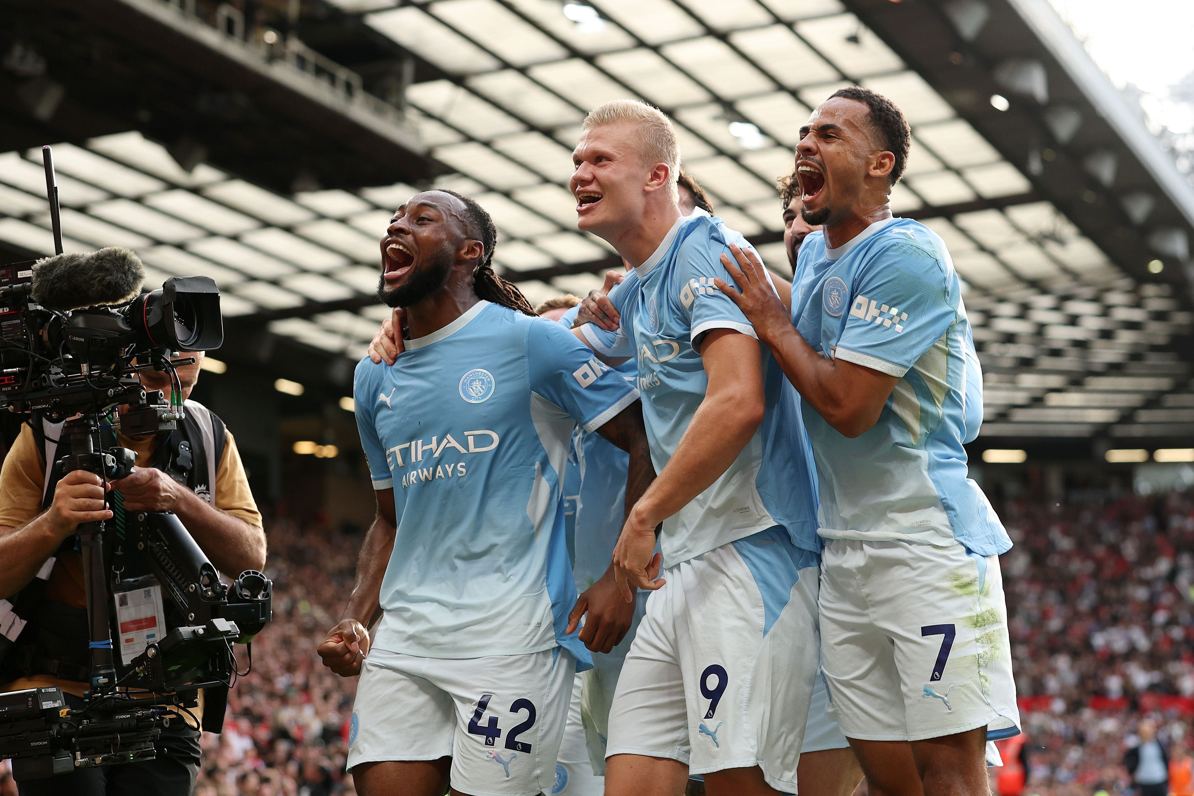 Drei jubelnde Manchester City-Spieler feiern ein Tor vor einer Fernsehkamera im Stadion.