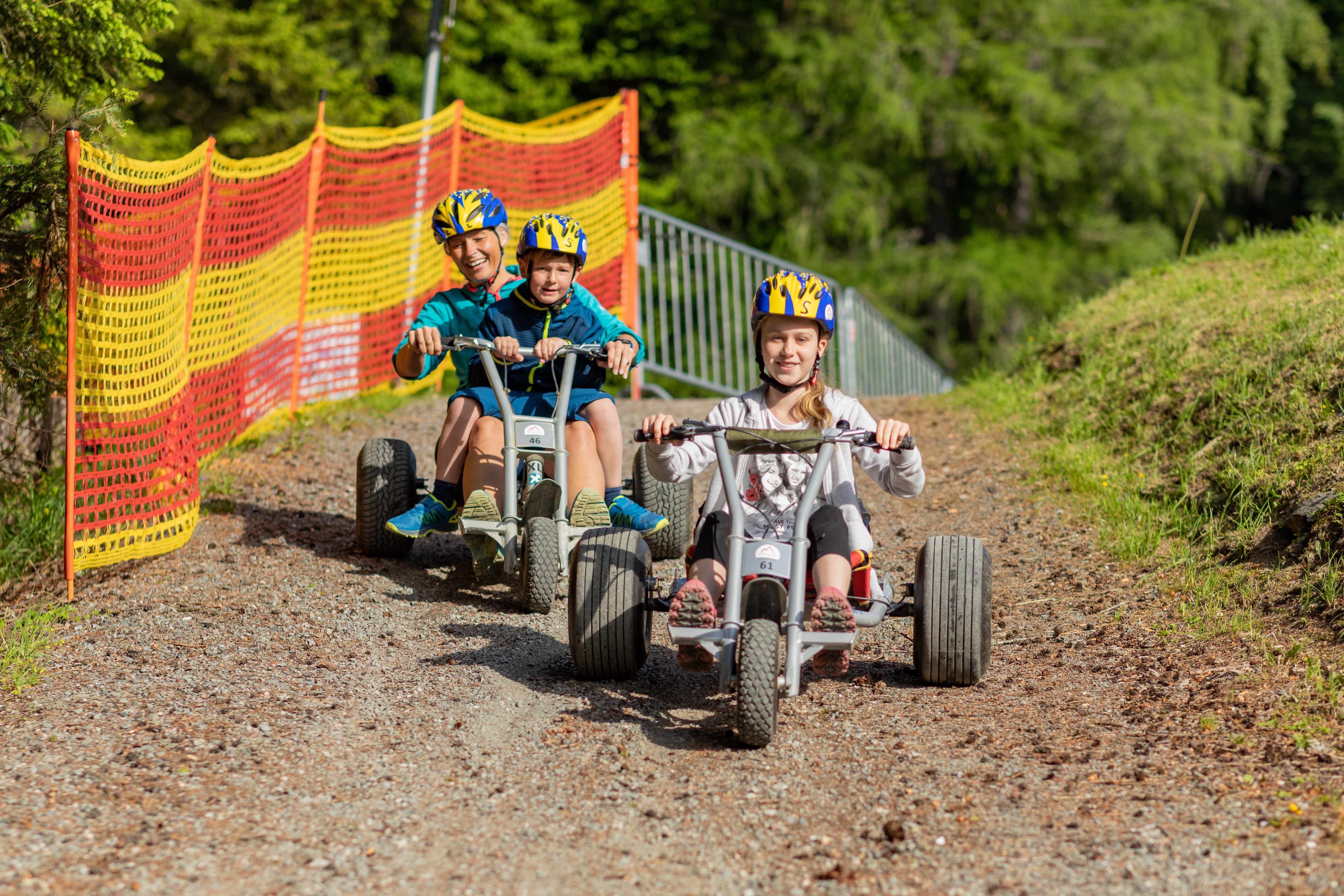 Drei Kinder fahren mit Kettcars bergab auf einem Schotterweg in Mönichkirchen.