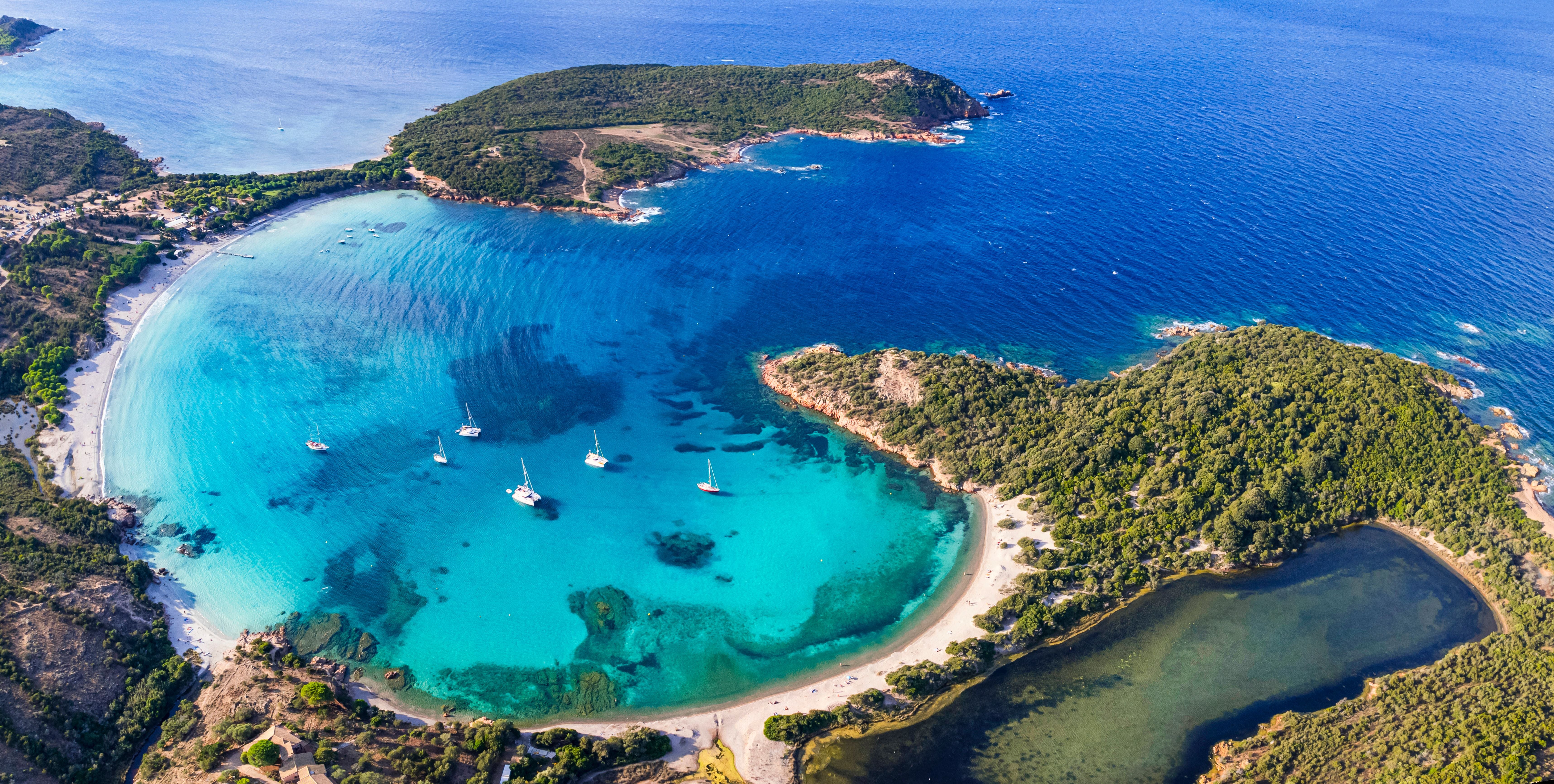 Luftaufnahme des Rondinara-Strandes auf Korsika mit türkisblauem Wasser und Segelbooten.