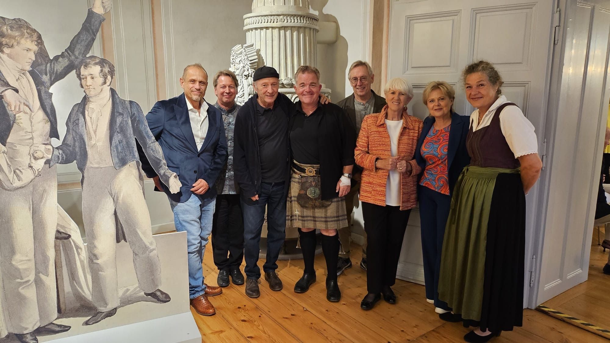 Eine Gruppe Erwachsener posiert lächelnd bei einer Veranstaltung vor einer historischen Kulisse.