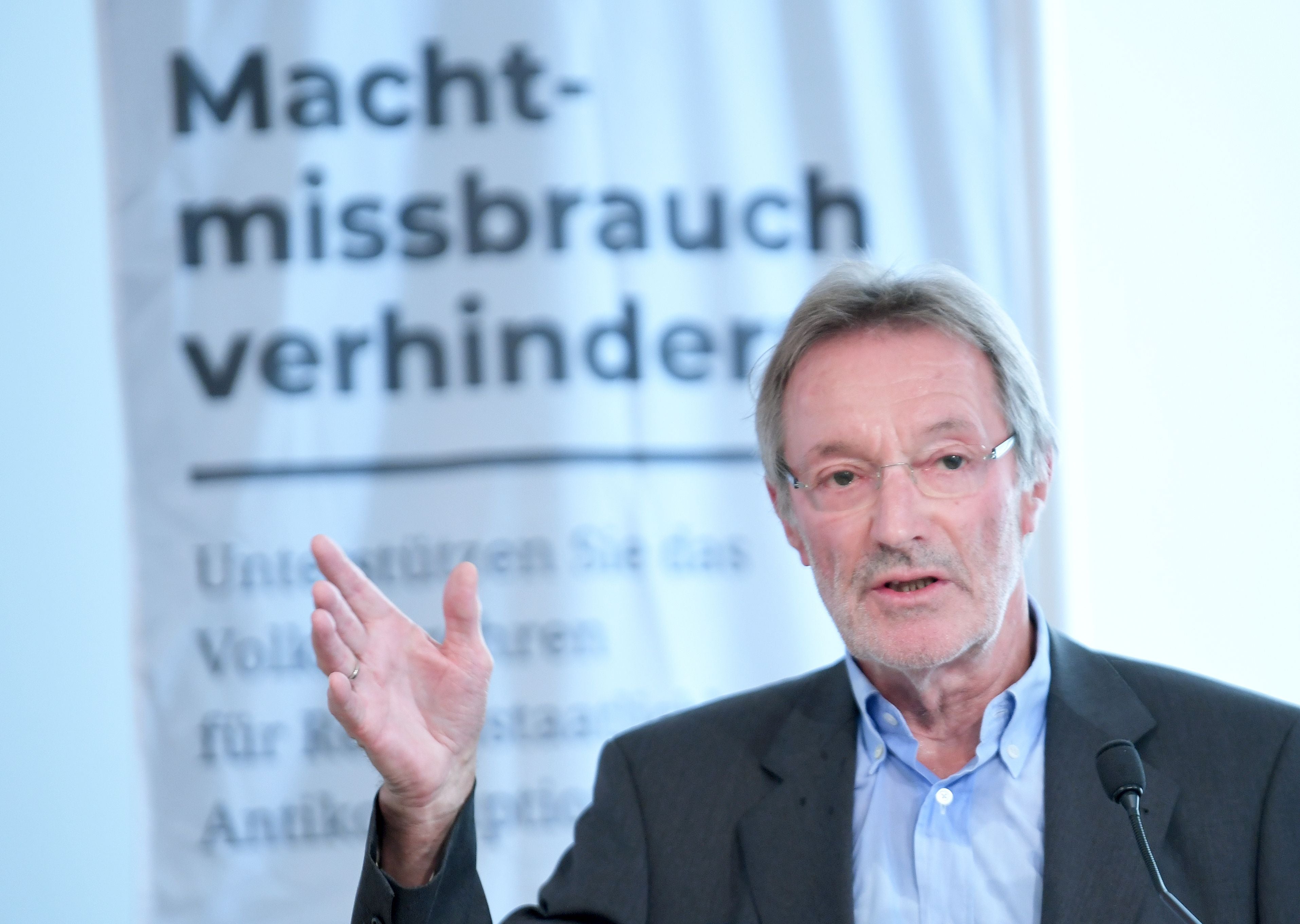 Ein Mann spricht bei einer Pressekonferenz vor einem Banner mit der Aufschrift „Machtmissbrauch verhindern“.