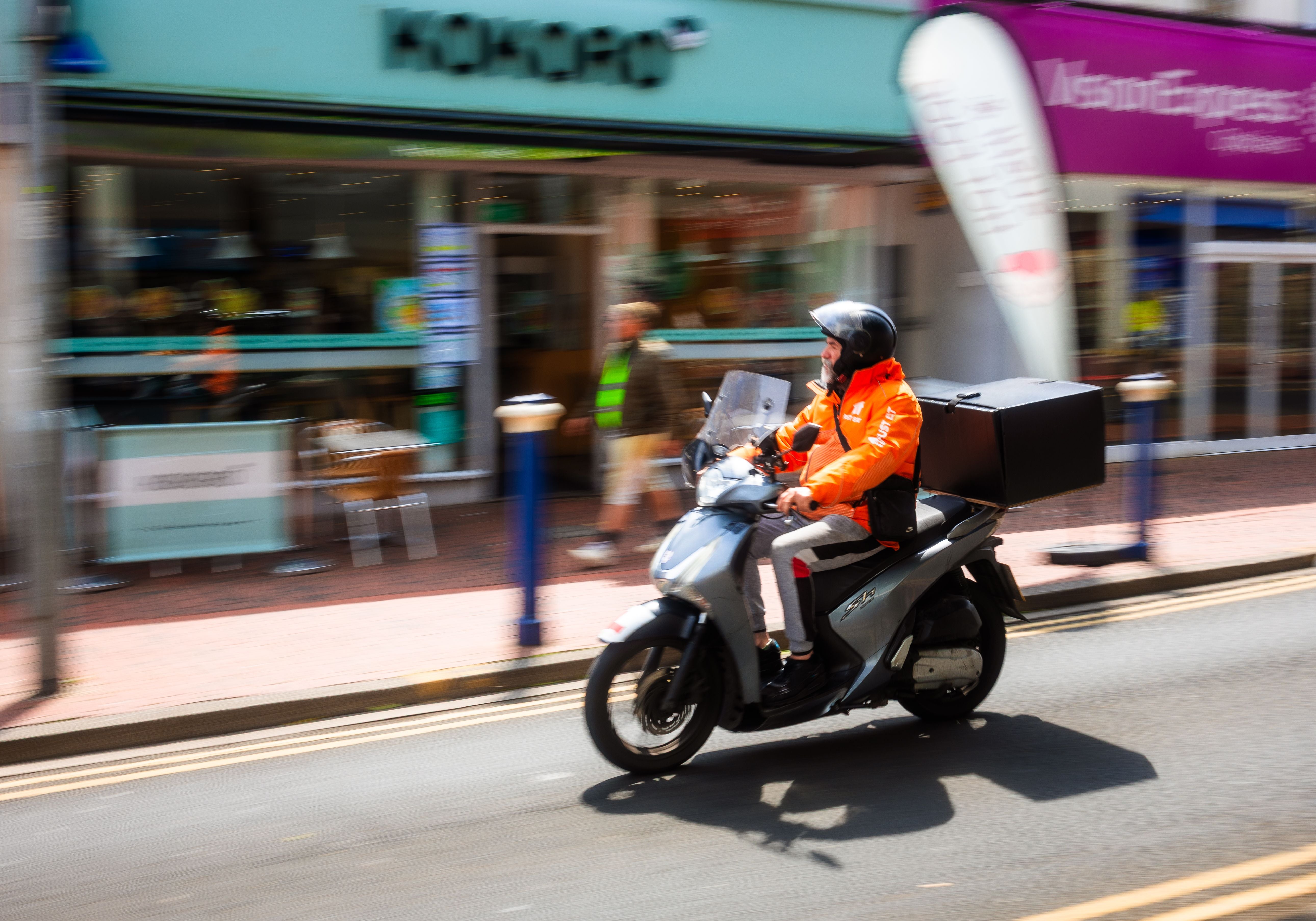 Ein Just Eat-Lieferfahrer fährt auf einem Motorrad durch eine Straße in Eastbourne, England.