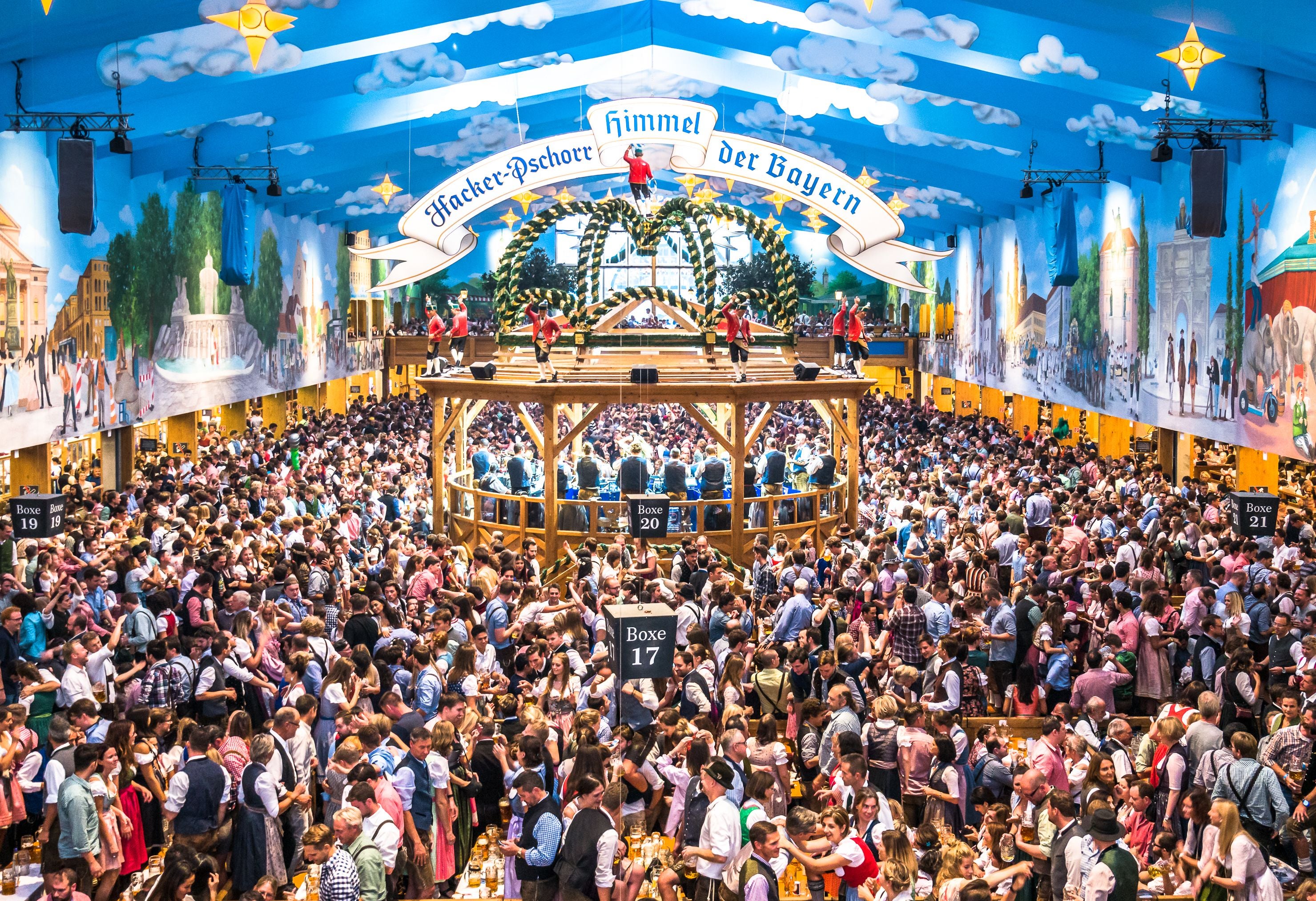 Große Menschenmenge in einem Festzelt beim Oktoberfest, viele in Tracht, mit Musikbühne und Dekoration.