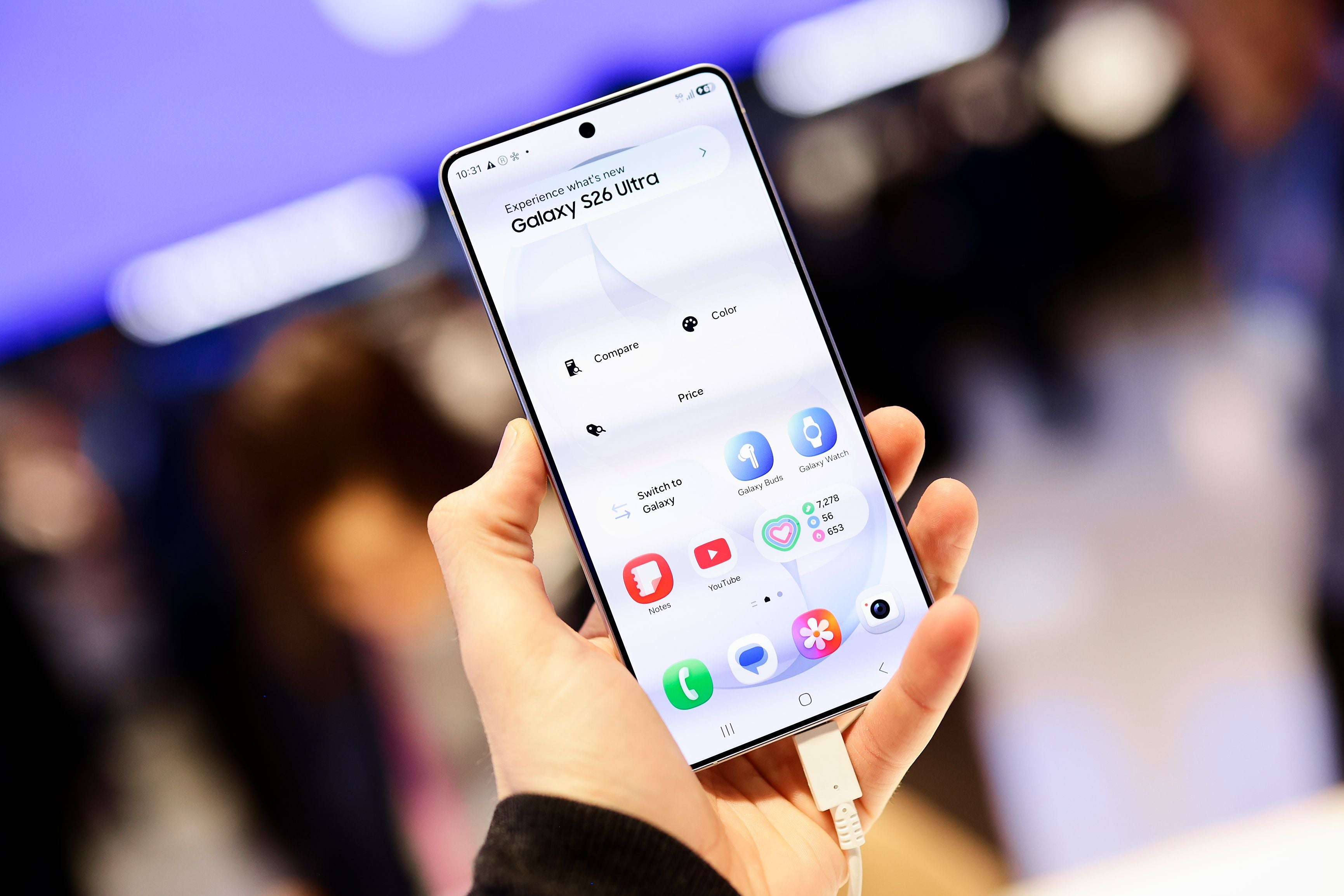 Eine Hand hält ein Samsung Galaxy S26 Ultra Smartphone mit Startbildschirm auf einer Messe.