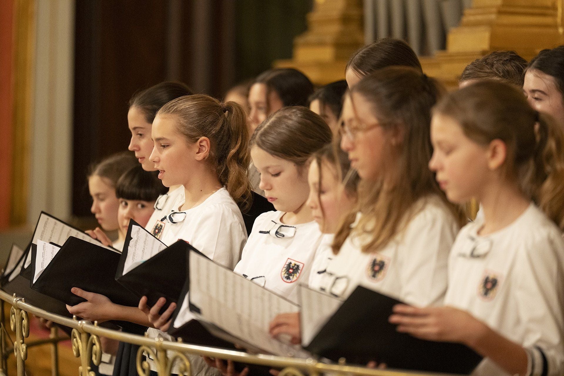 Mehrere Mädchen im Chor mit Noten in den Händen singen gemeinsam in weißen Uniformen.