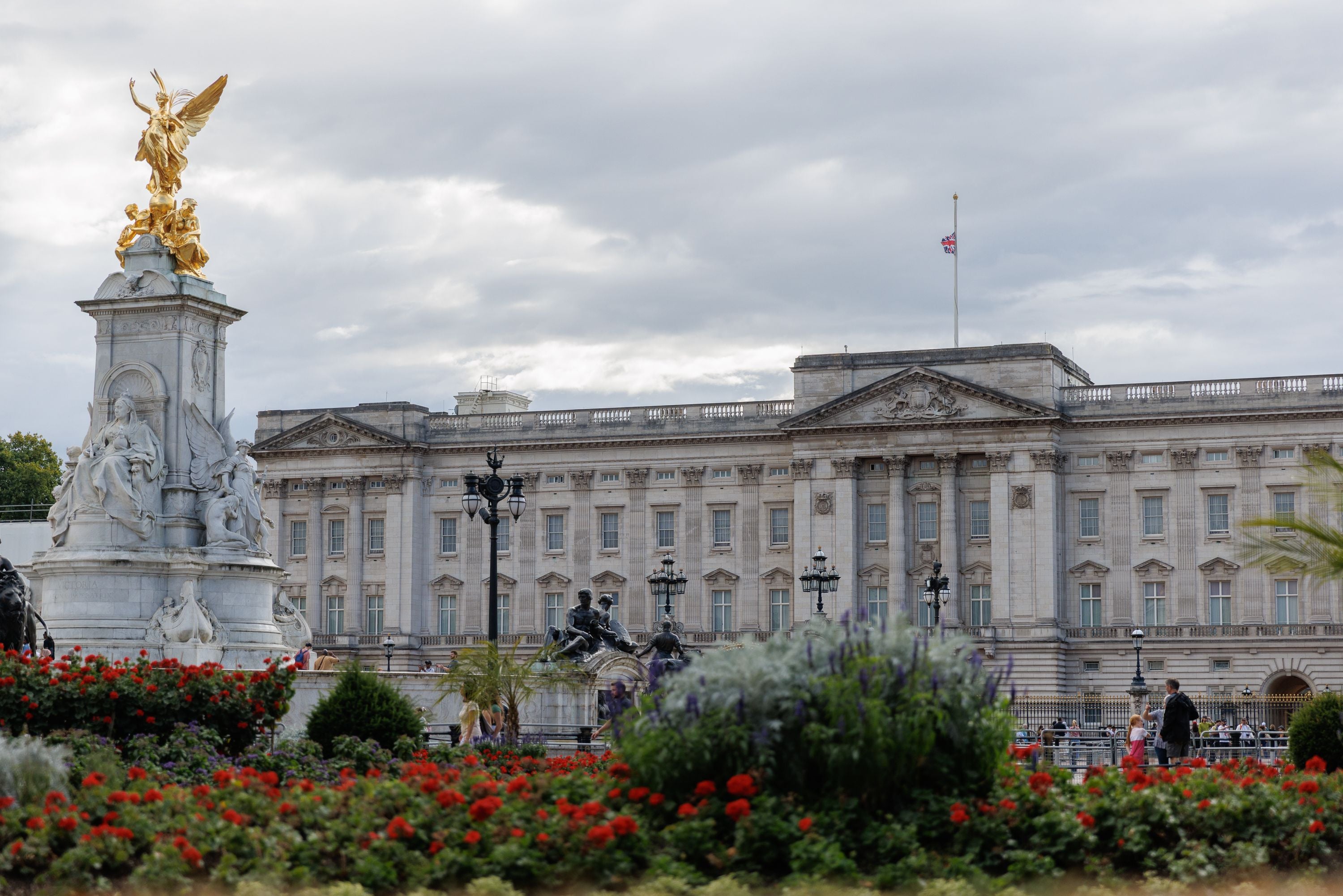 Buckingham Palace mit Halbmastflagge, Victoria-Denkmal im Vordergrund und Blumenbeeten.