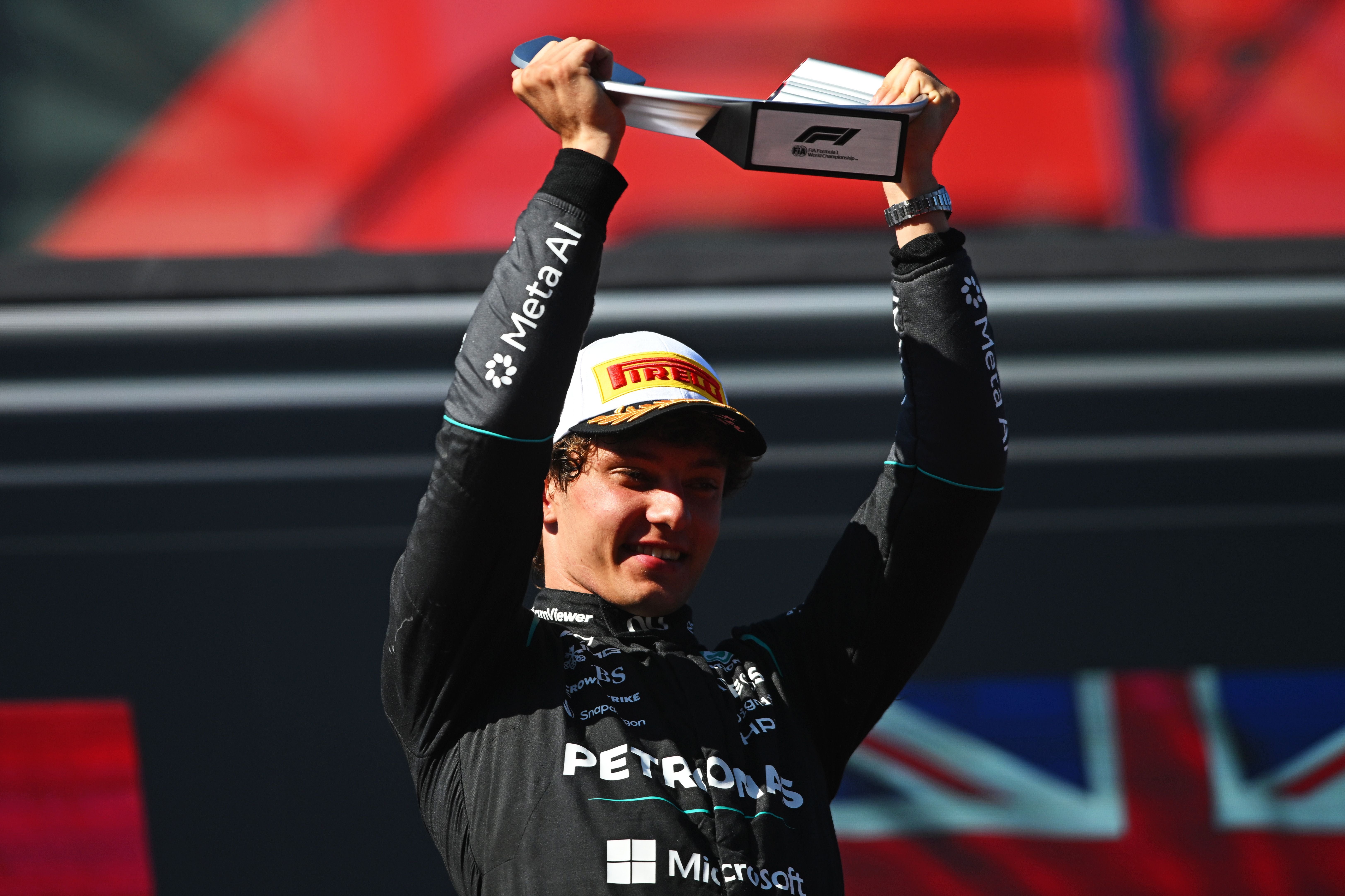 Ein Rennfahrer jubelt auf dem Podium und hält einen Pokal über dem Kopf.