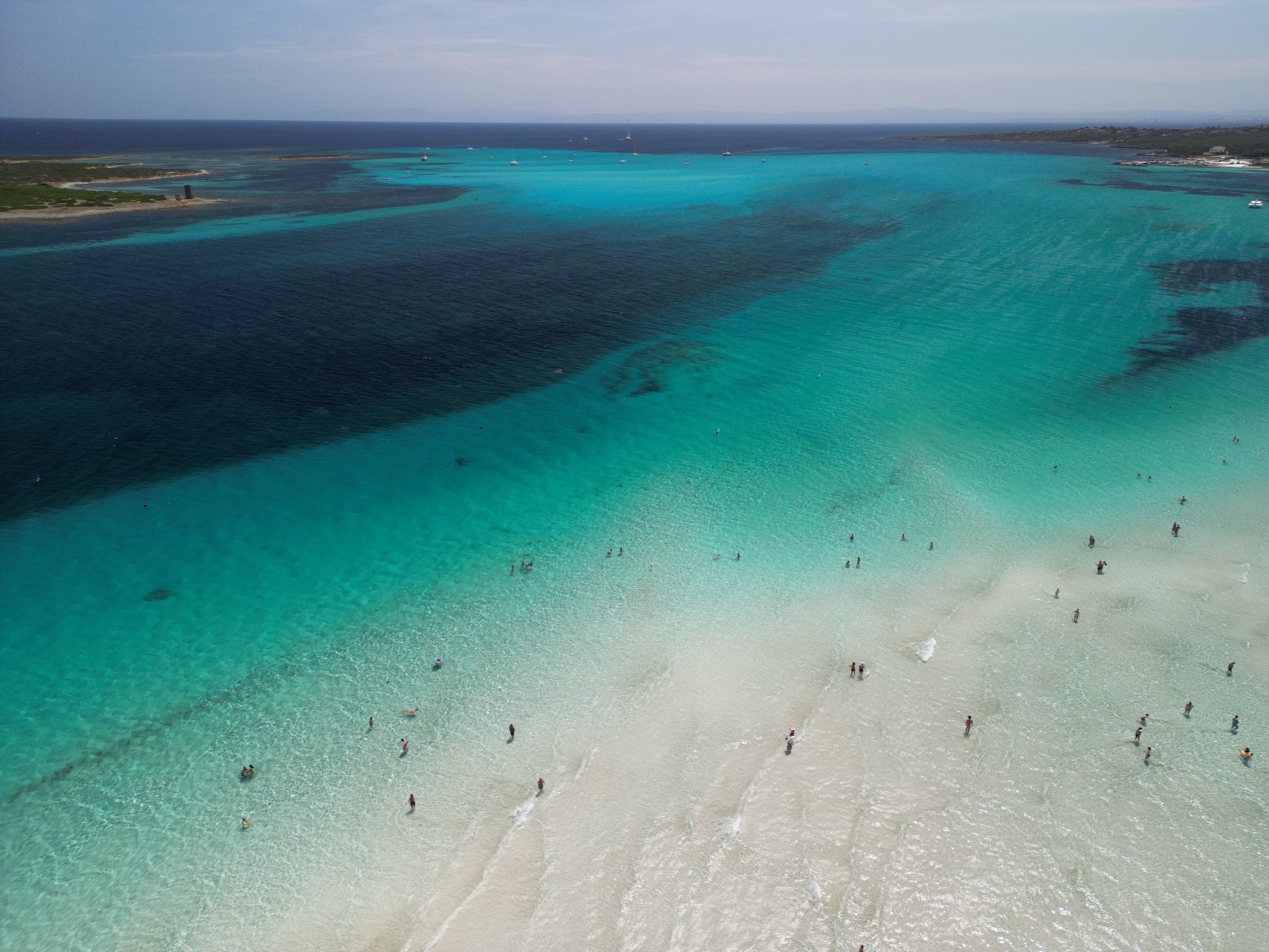 Luftaufnahme des Strands La Pelosa auf Sardinien mit türkisfarbenem Wasser und Badenden.