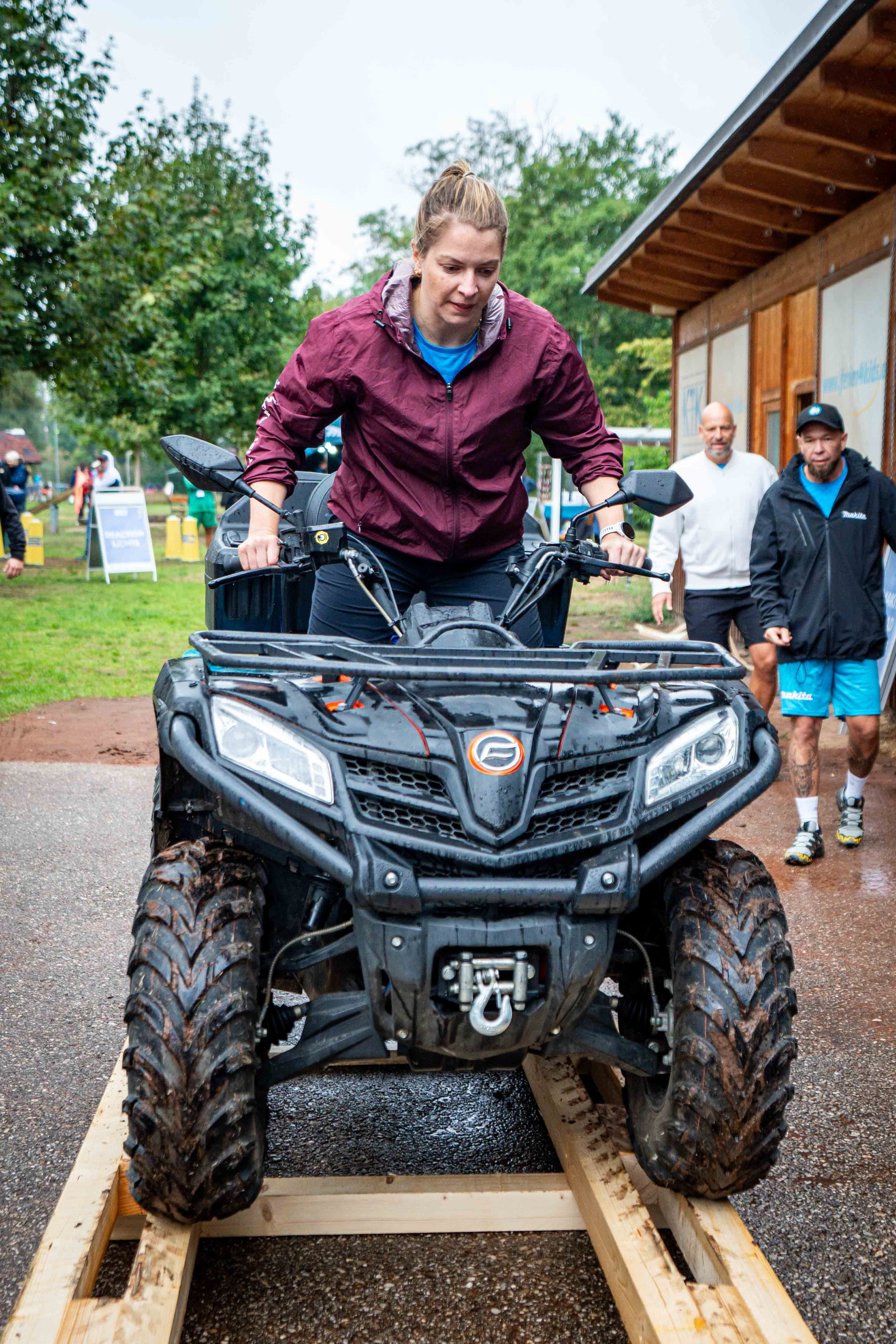 Eine Frau fährt ein Quad auf Holzplanken bei einer Outdoor-Teamchallenge.