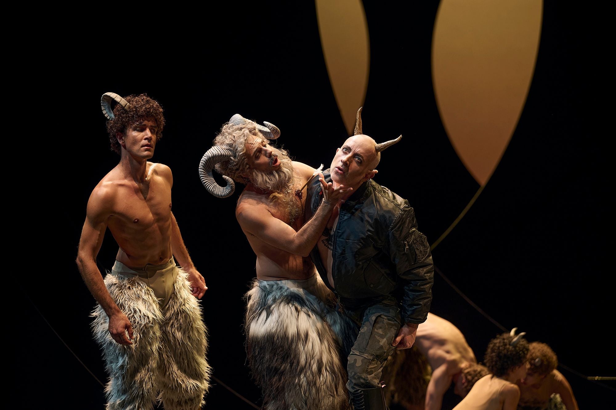 Drei Männer in Ziegenkostümen und Hörnern spielen auf einer Theaterbühne.