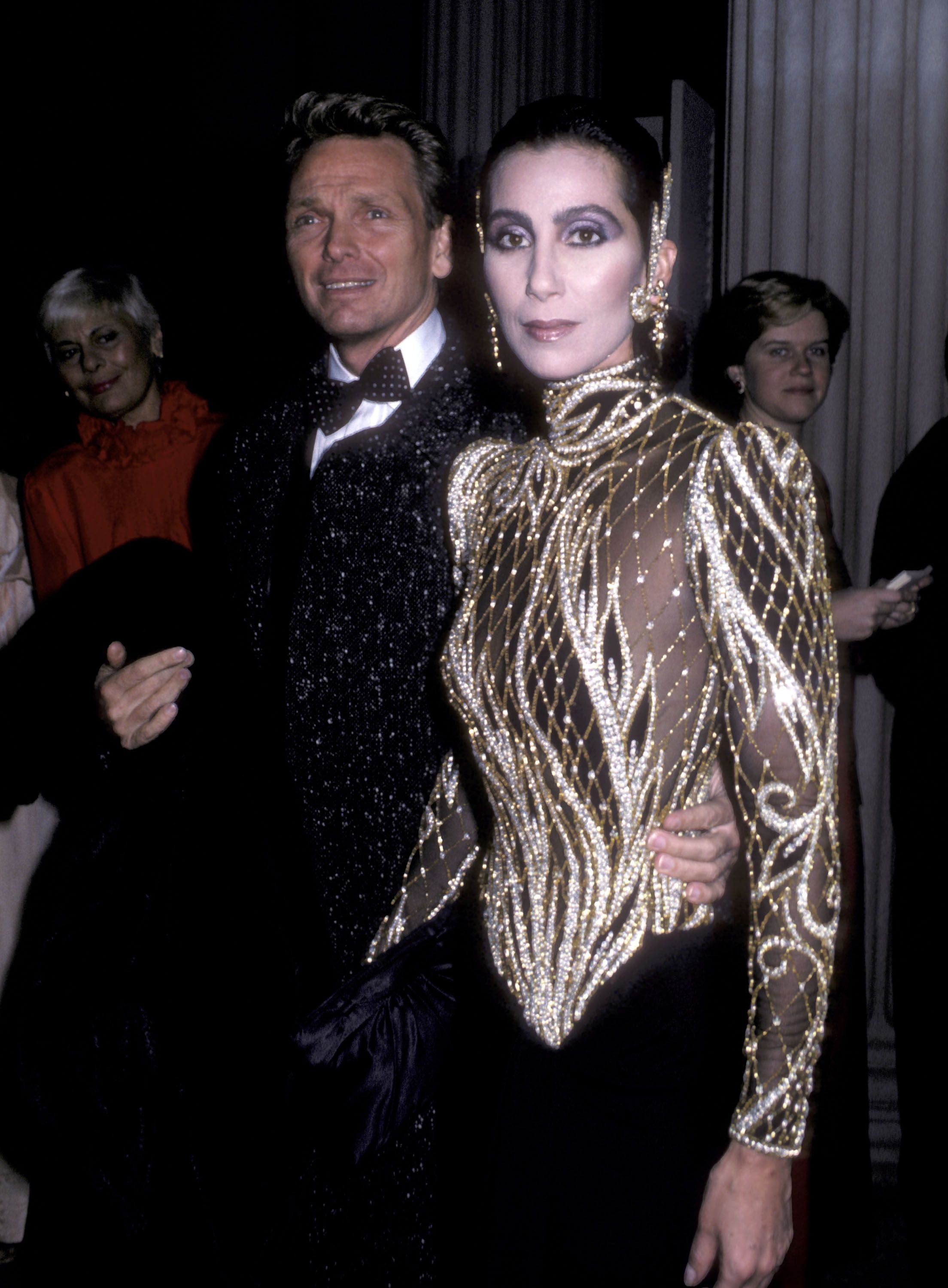 Elegant gekleidetes Paar posiert auf einer Gala, Frau trägt glitzerndes, goldenes Kleid.