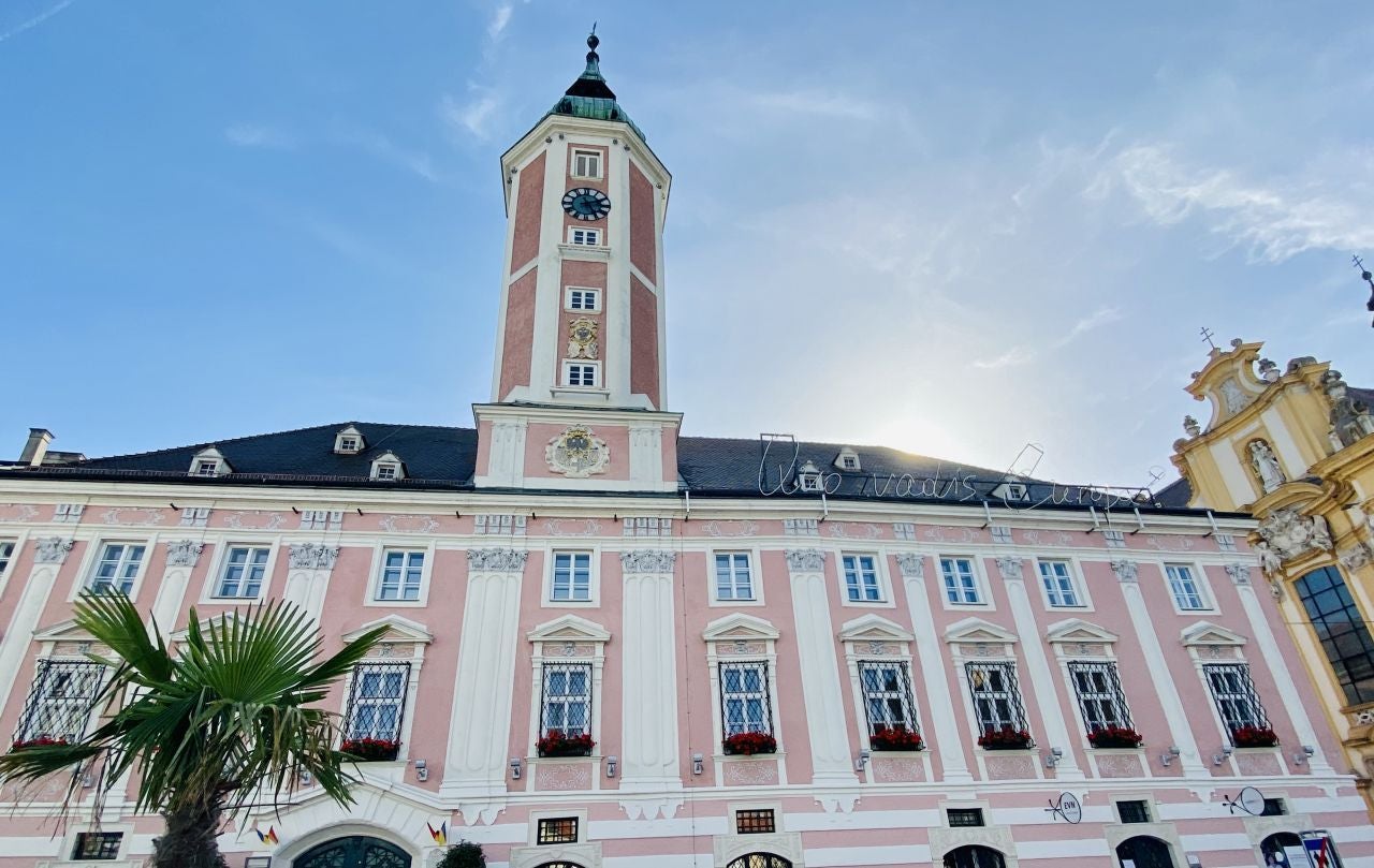 Das rosa-weiße Rathaus von St. Pölten mit Uhrturm bei Sonnenschein und blauem Himmel.