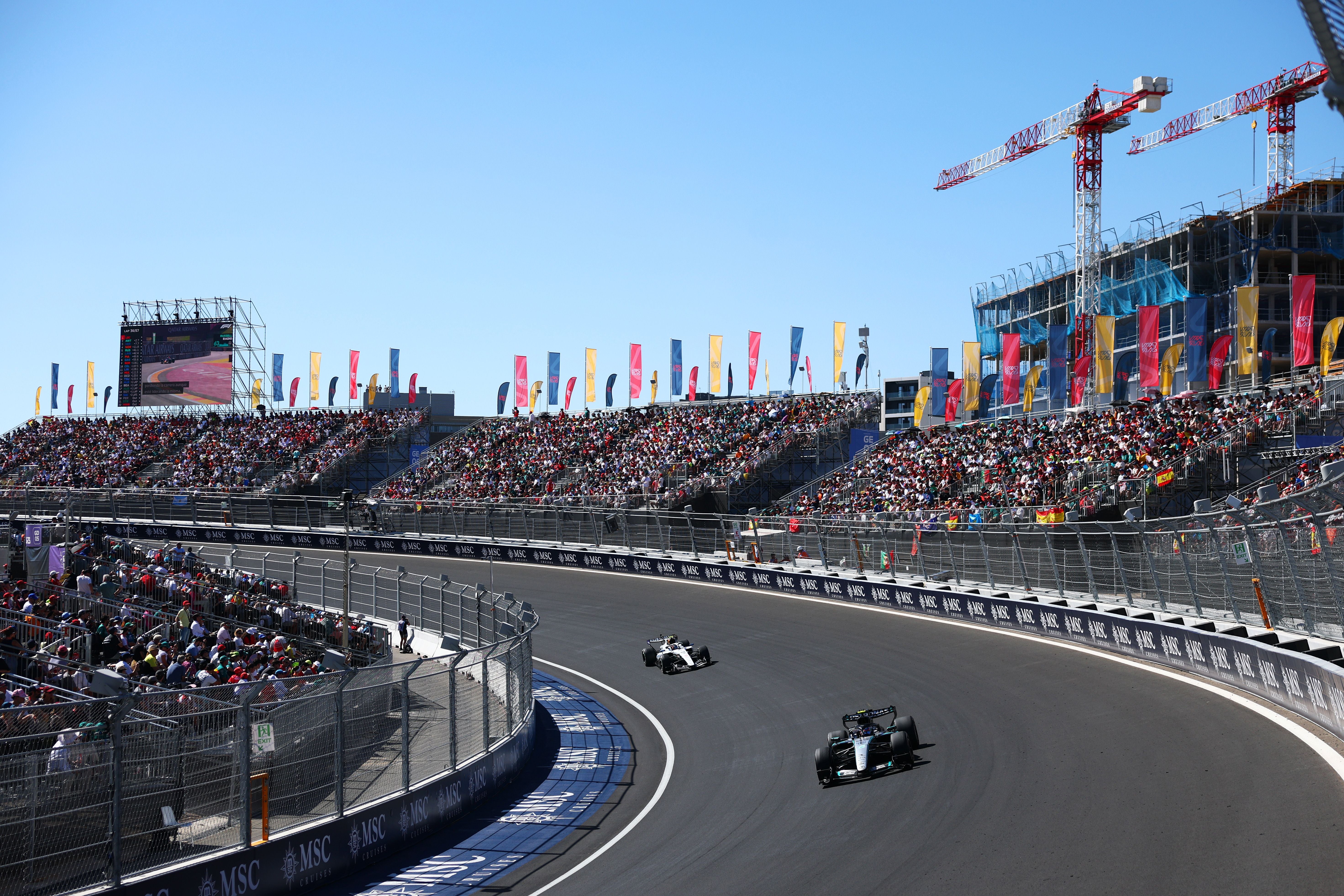 Zwei Formel-1-Autos fahren auf einer Rennstrecke vor vollen Tribünen und bunten Fahnen.