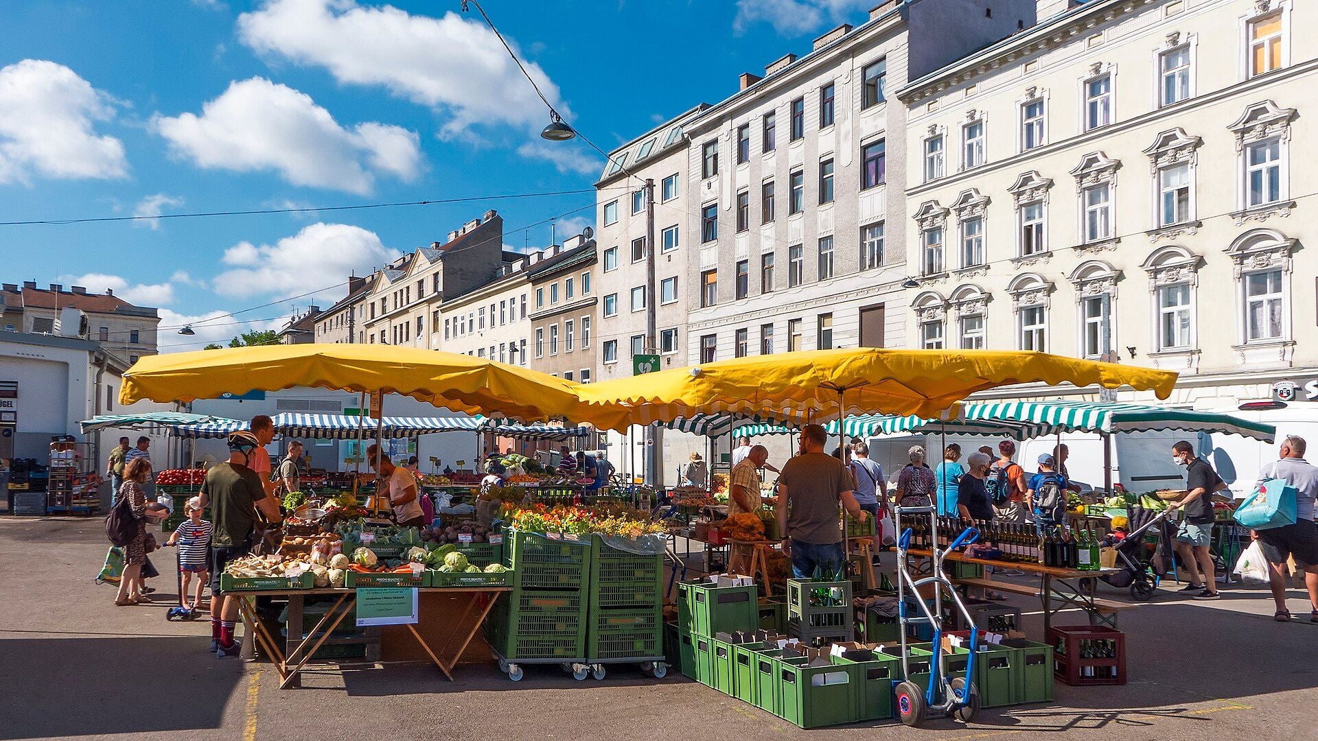 Menschen kaufen unter gelben Sonnenschirmen auf dem Hannovermarkt frisches Obst und Gemüse ein.