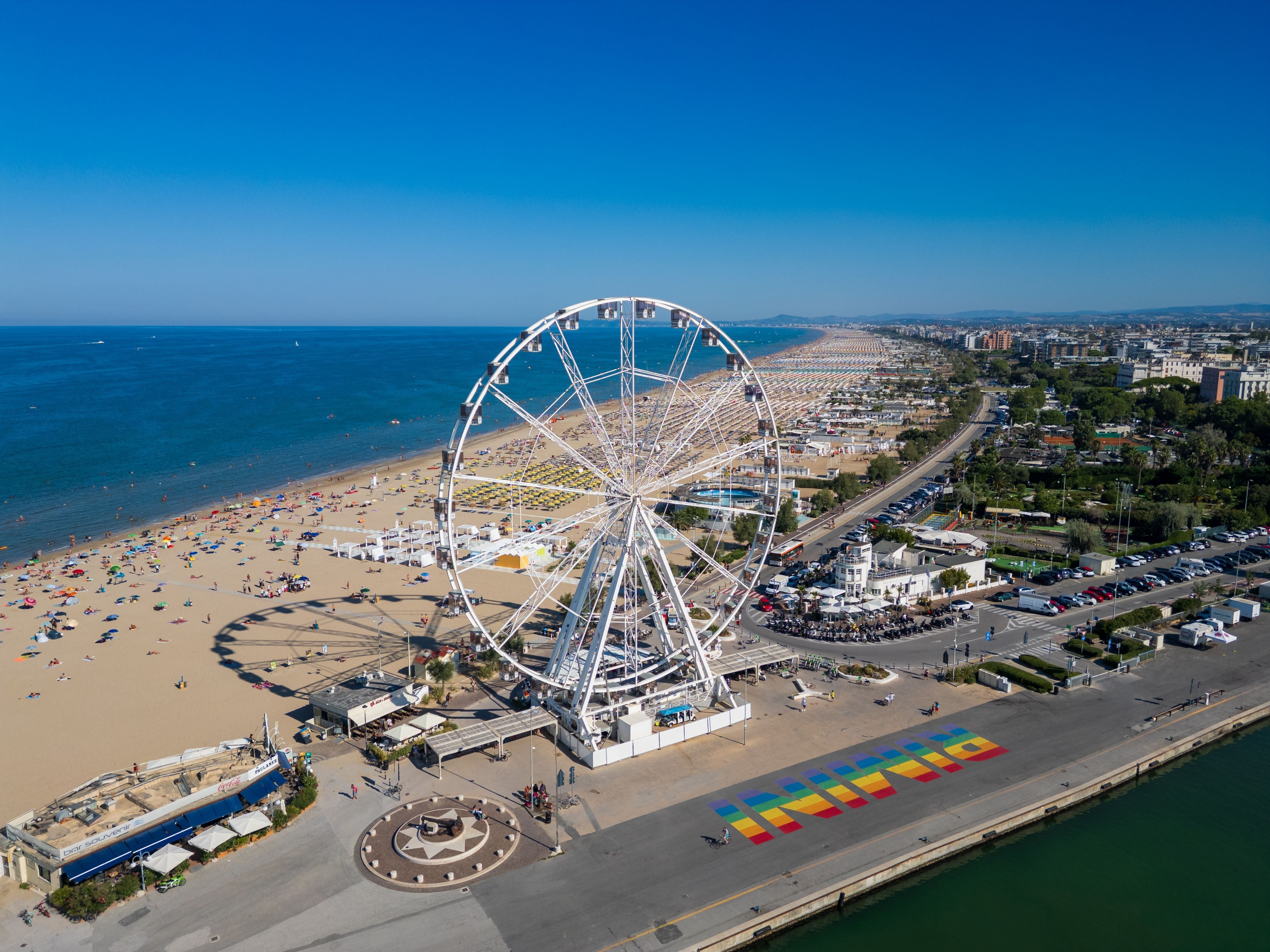 Luftaufnahme vom Strand von Rimini mit Riesenrad, bunten Sonnenschirmen und dem Adriatischen Meer.
