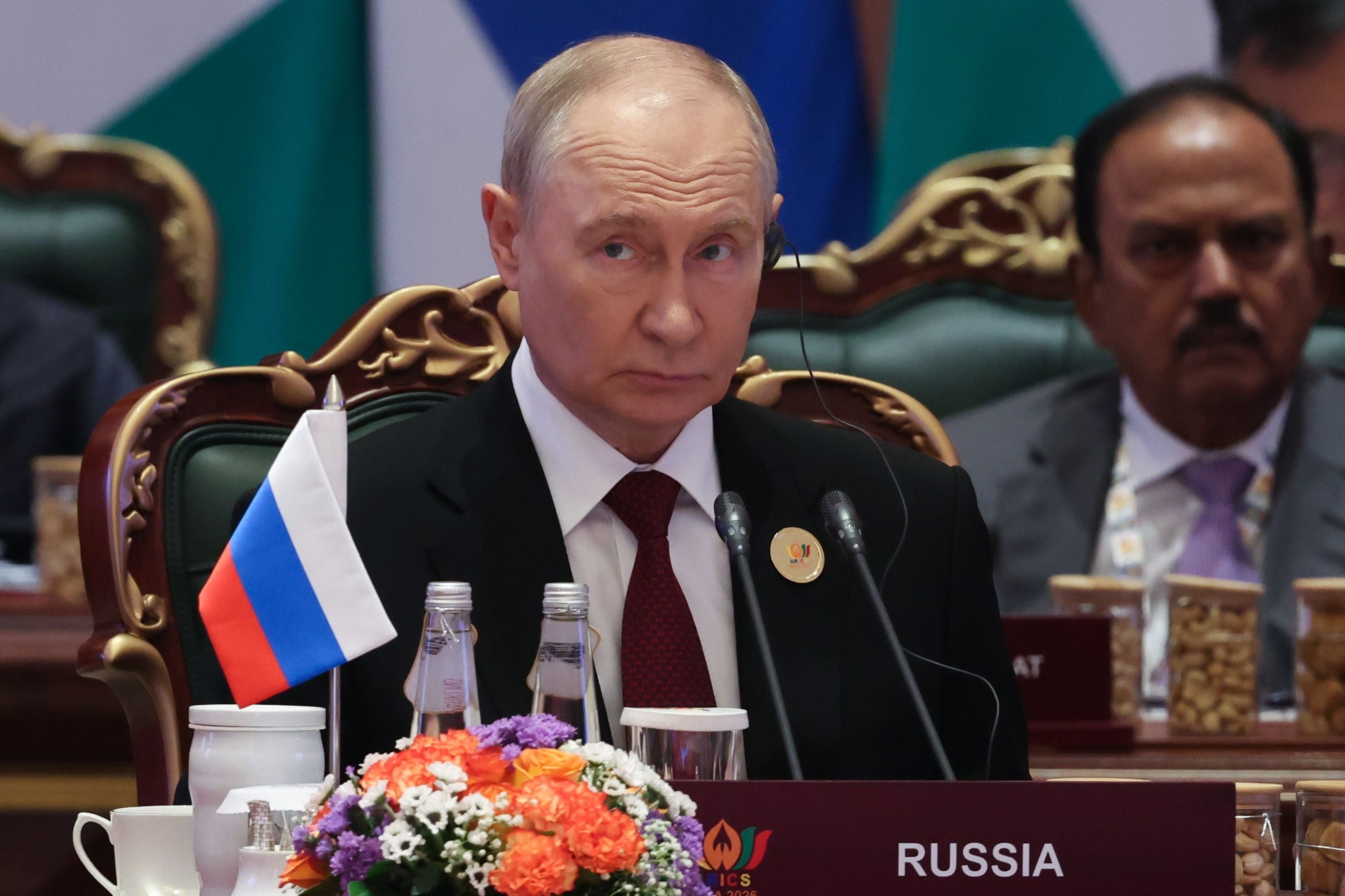 Der russische Präsident sitzt mit russischer Flagge und Blumenarrangement bei einem BRICS-Gipfel.