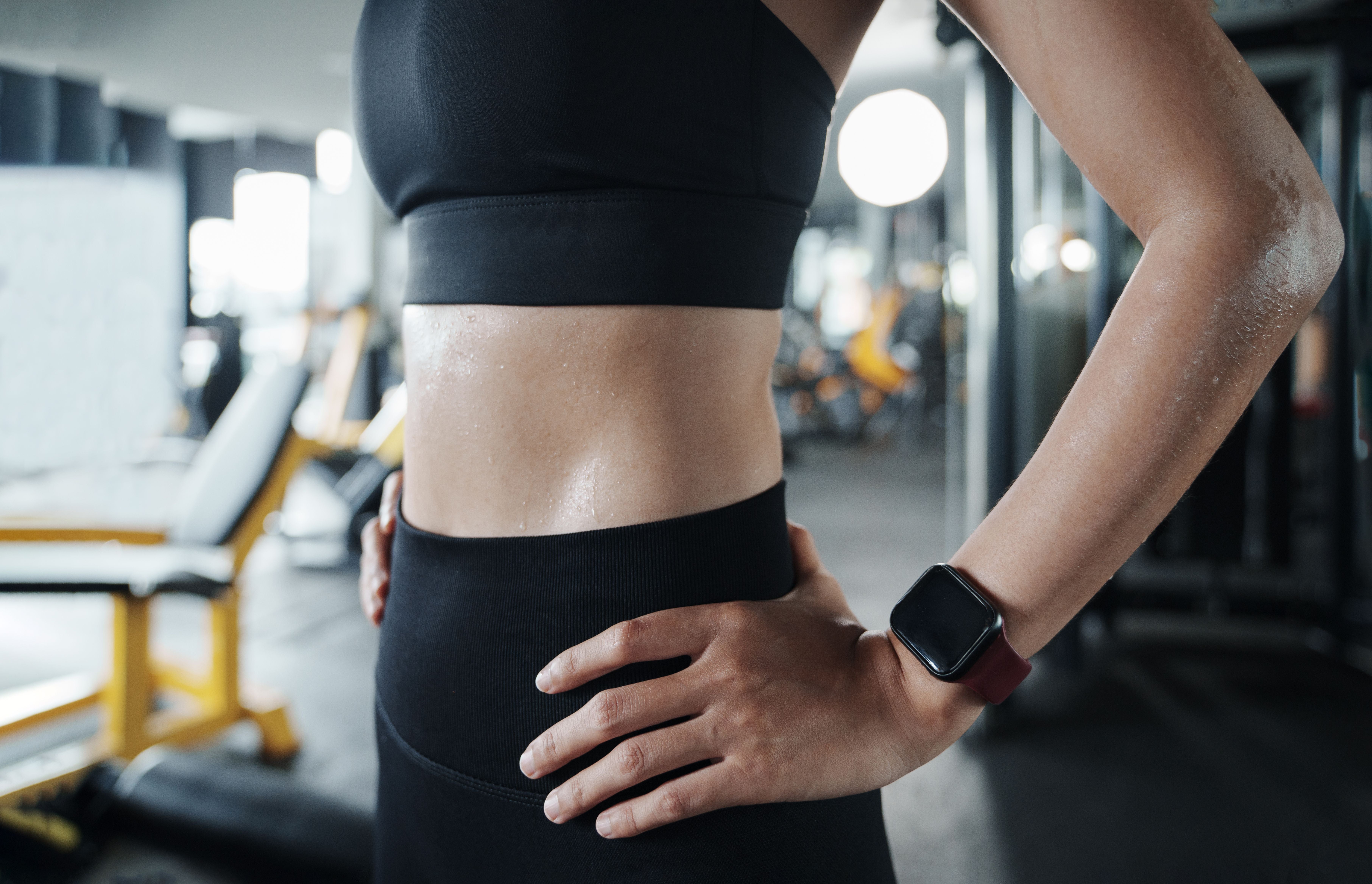 Verschwitze Frau im Sport-BH stemmt die Hände in die Hüften, im Fitnessstudio.