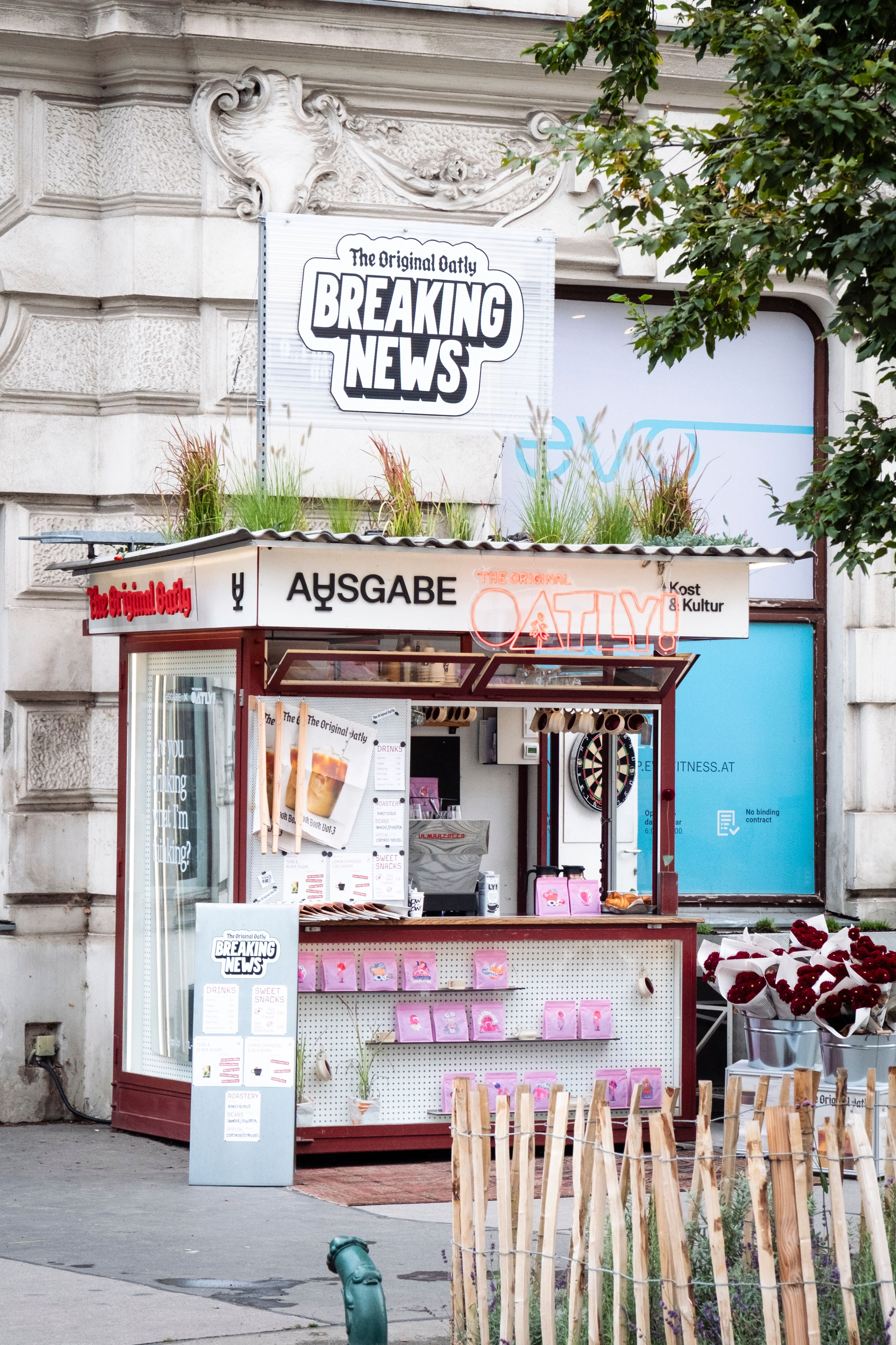 Oatly Pop-up-Kiosk mit "Breaking News"-Schild und Blumen auf dem Dach in einer Stadt.