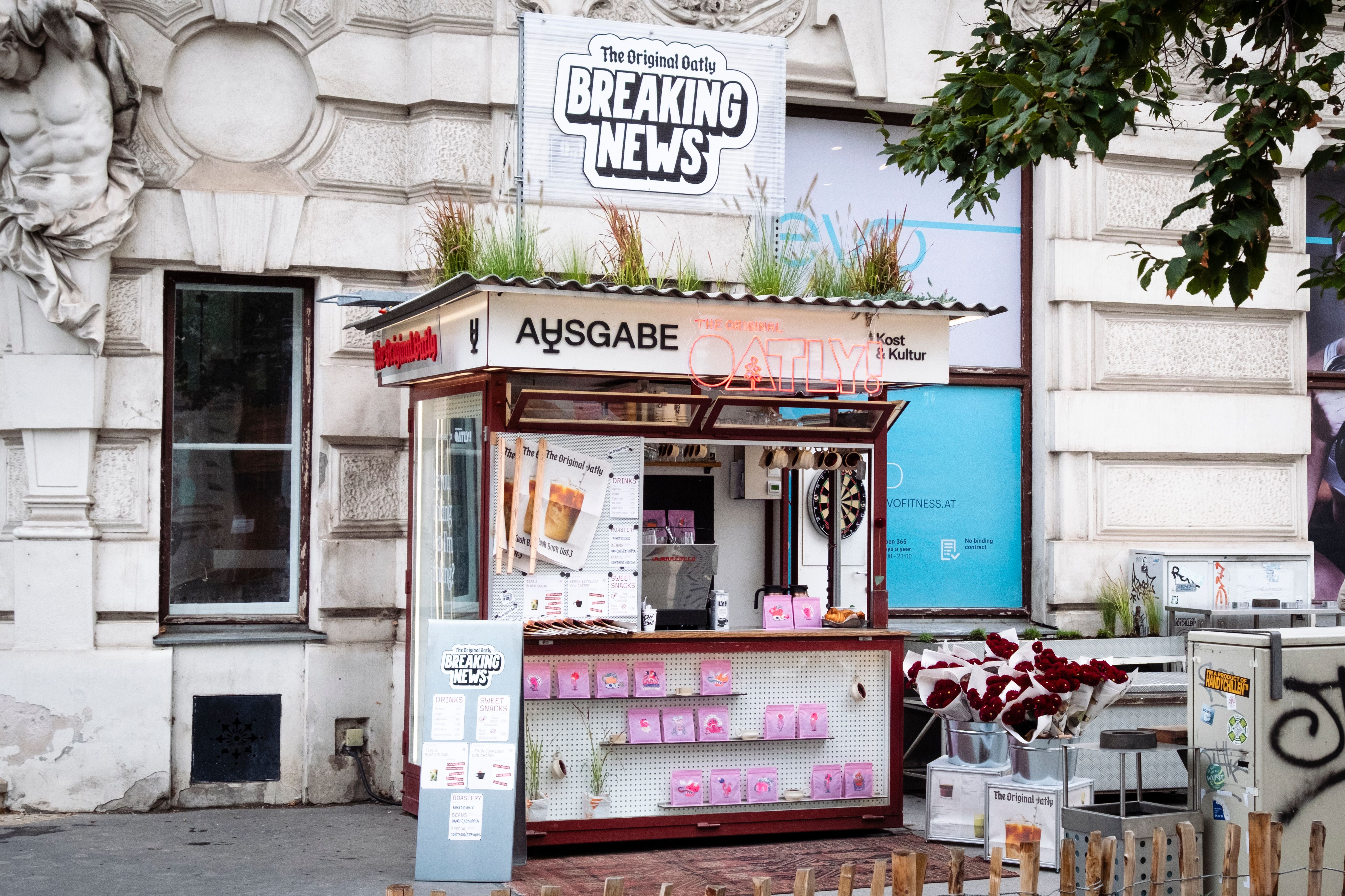 Kleiner Oatly-Pop-up-Stand mit Verkaufsfenster, Werbeschildern und Blumensträußen davor.