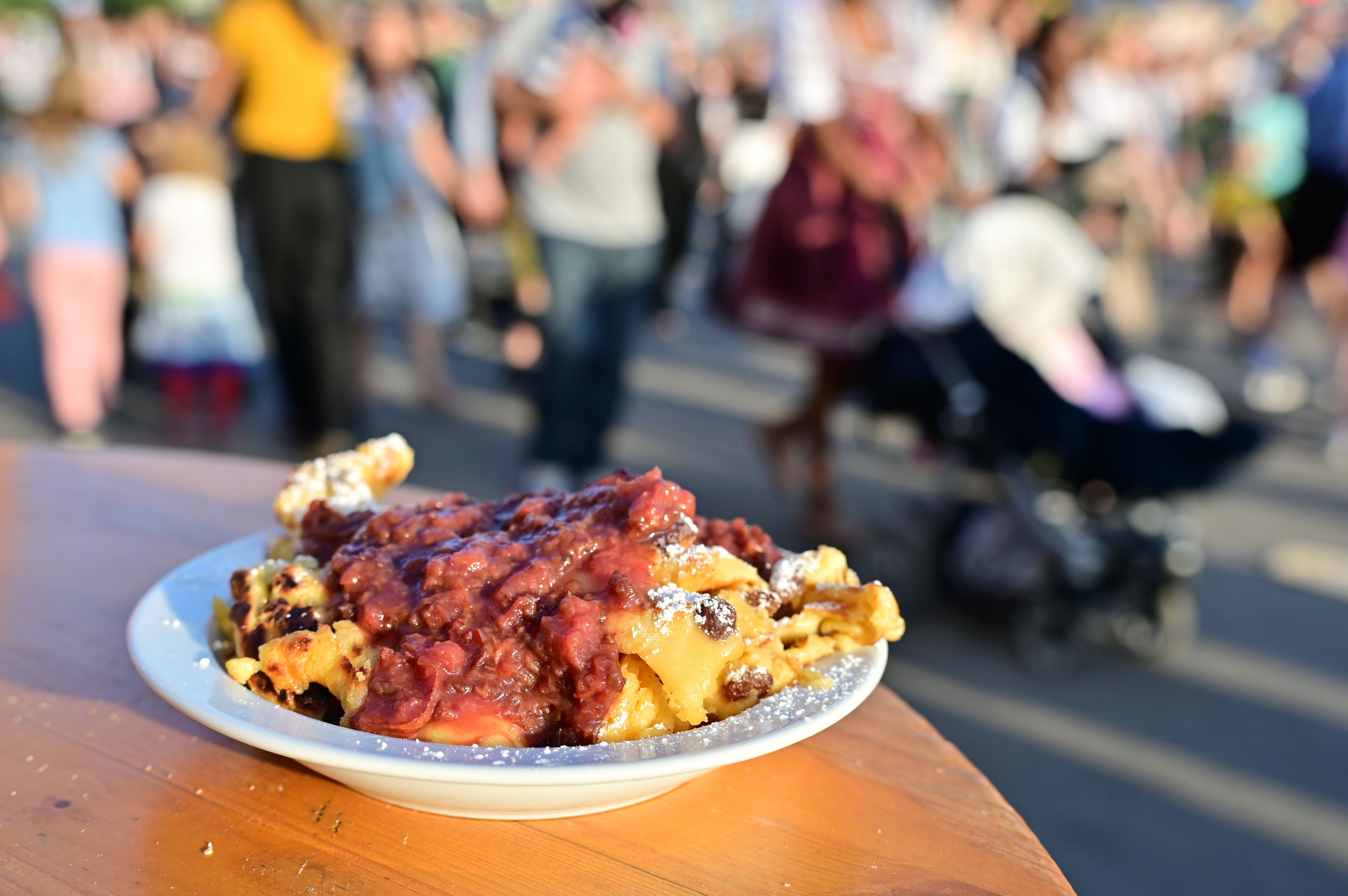 Kaiserschmarrn mit Puderzucker und Rosinen auf einem Teller, im Hintergrund Oktoberfest-Besucher.