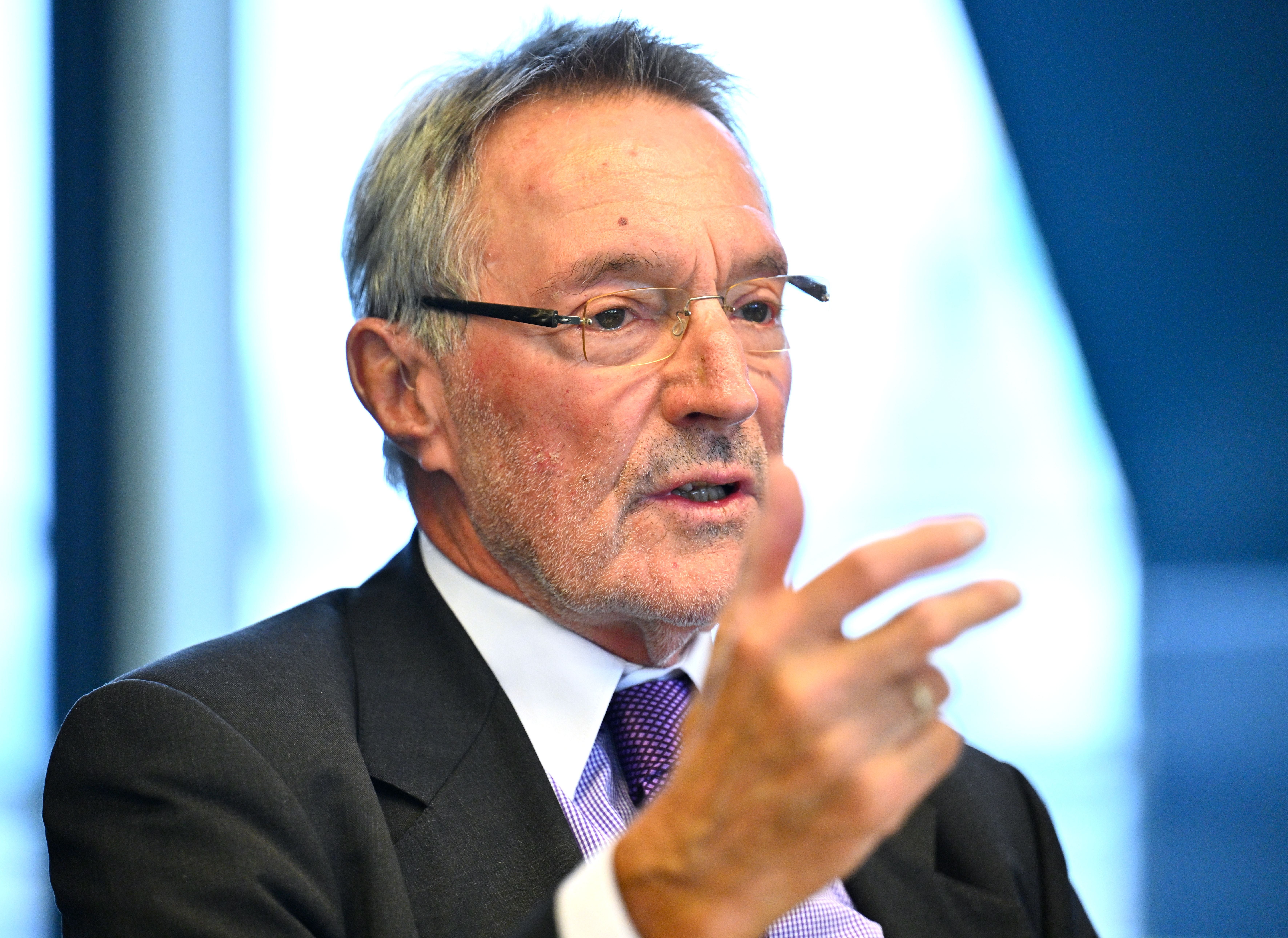 Ein älterer Mann im Anzug spricht und gestikuliert während einer Pressekonferenz.