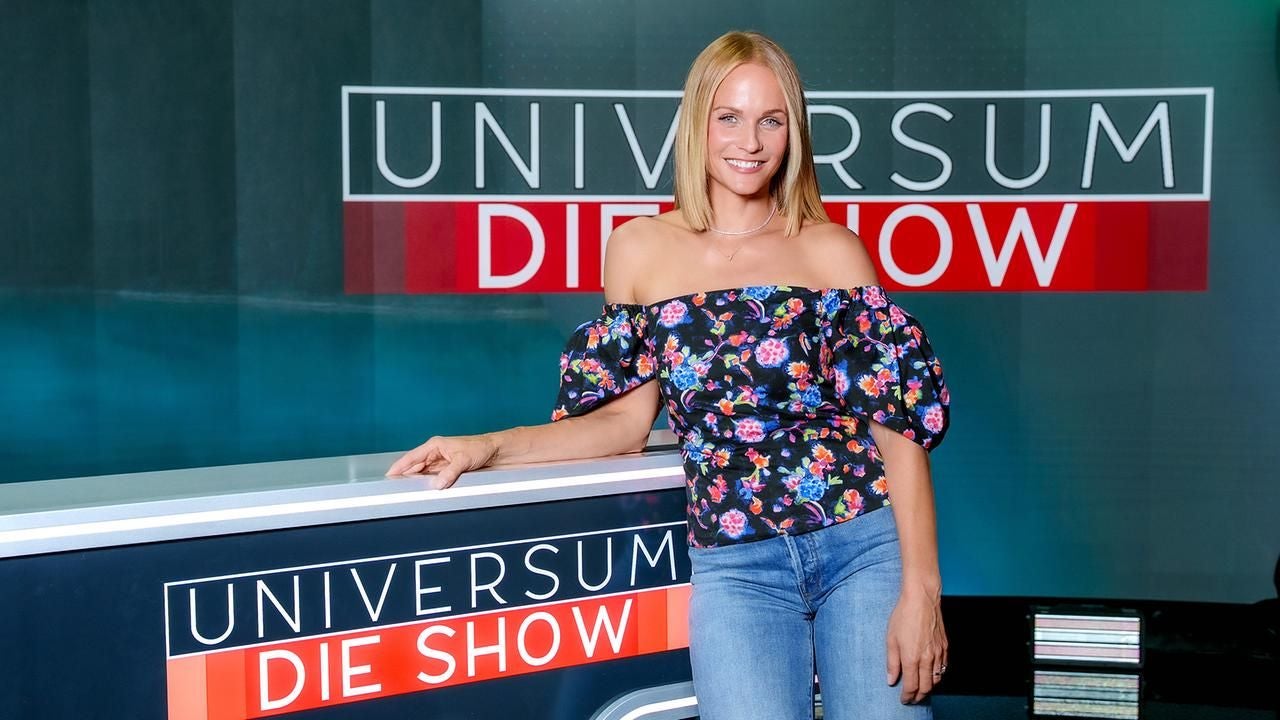 Frau in Jeans und Blumenbluse steht vor einem Tresen mit dem Schriftzug „Universum Die Show“.