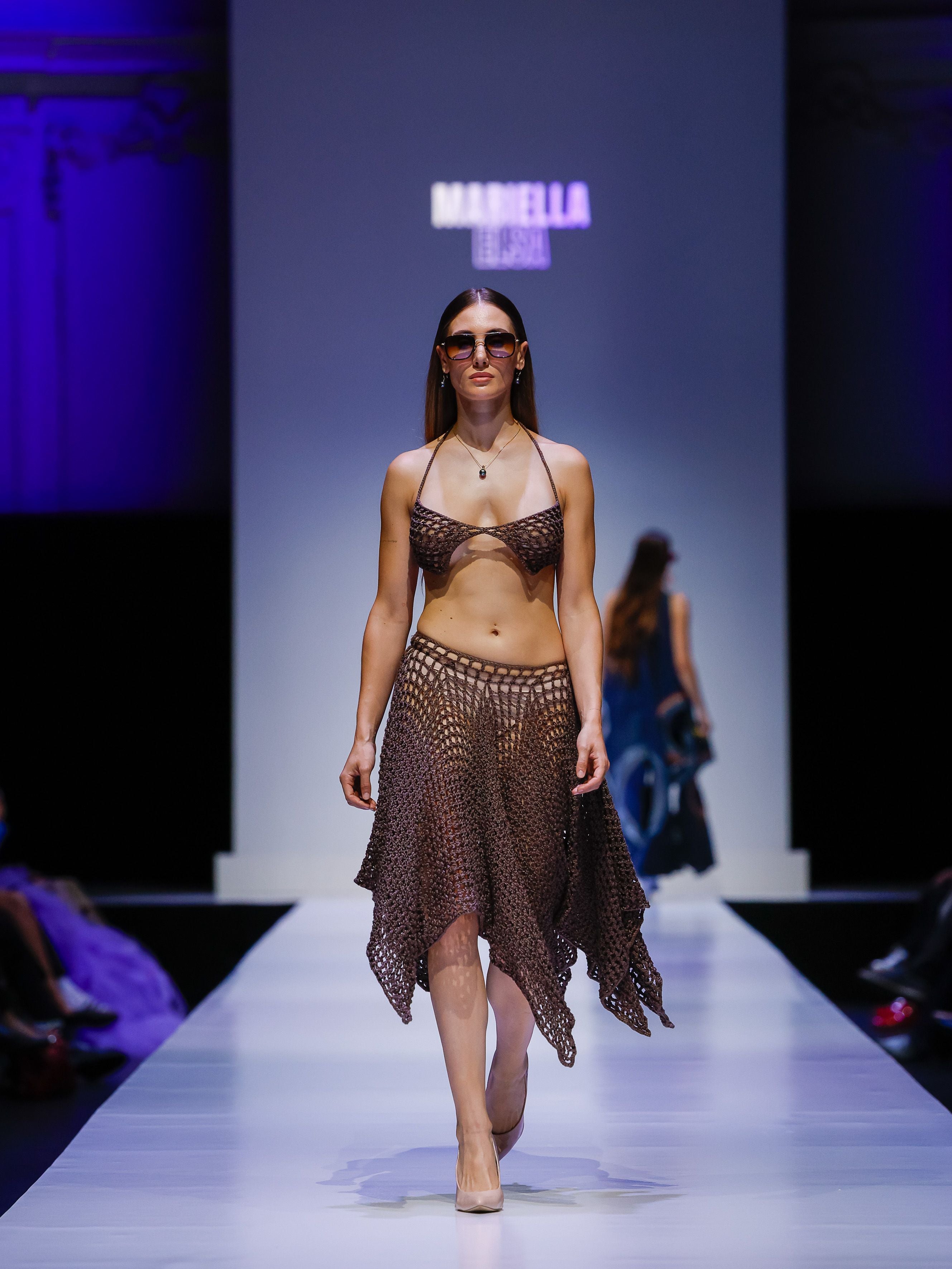 Model trägt ein gehäkeltes braunes Outfit und Sonnenbrille auf dem Laufsteg.