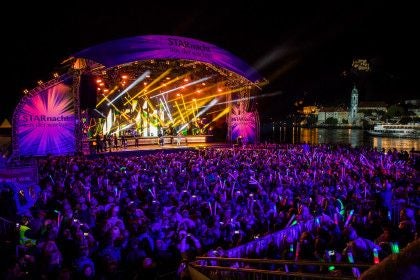 Großes Open-Air-Konzert bei Nacht mit beleuchteter Bühne und feierndem Publikum.