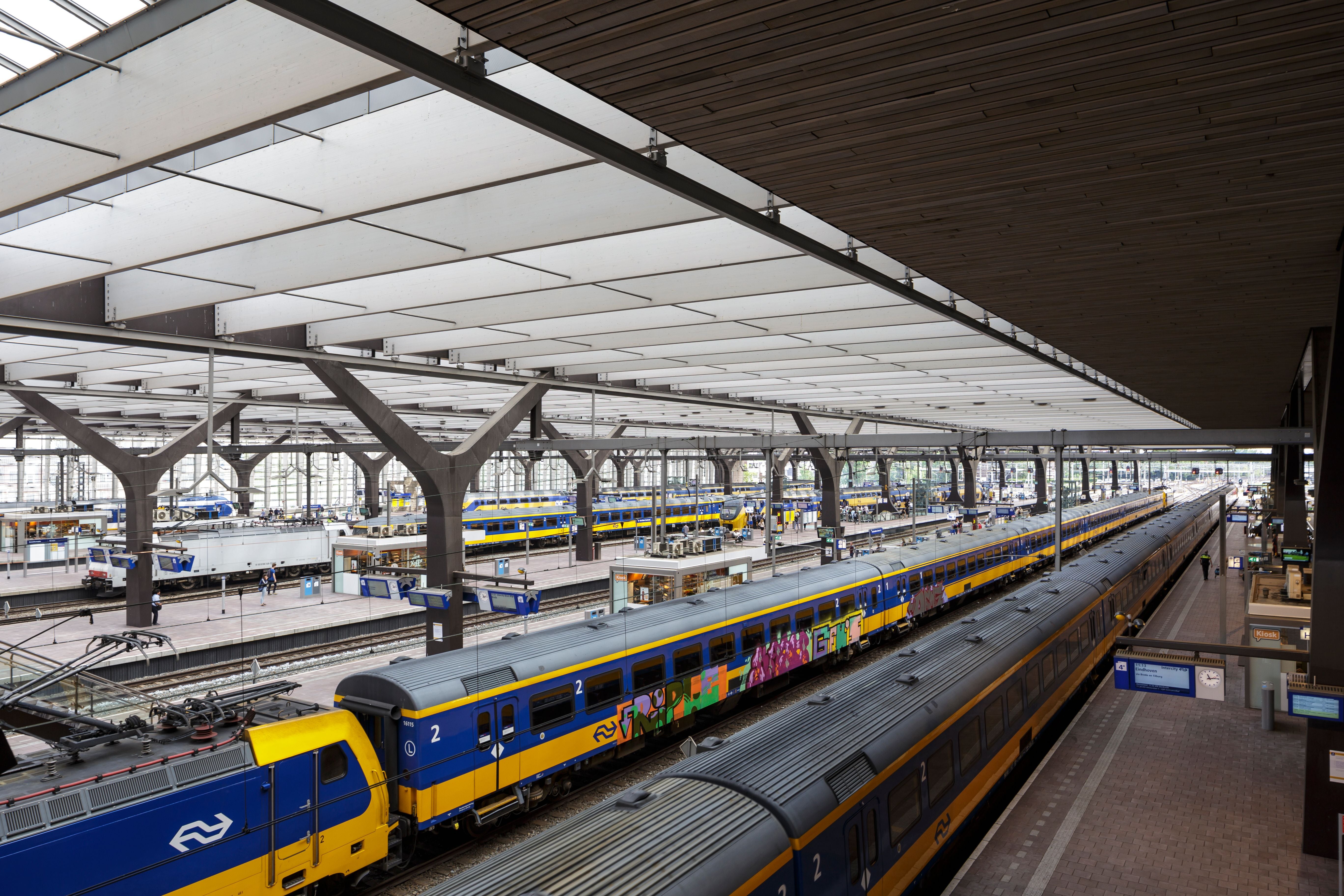 Mehrere blau-gelbe Züge stehen in einem modernen, überdachten Bahnhof mit Bahnsteigen.