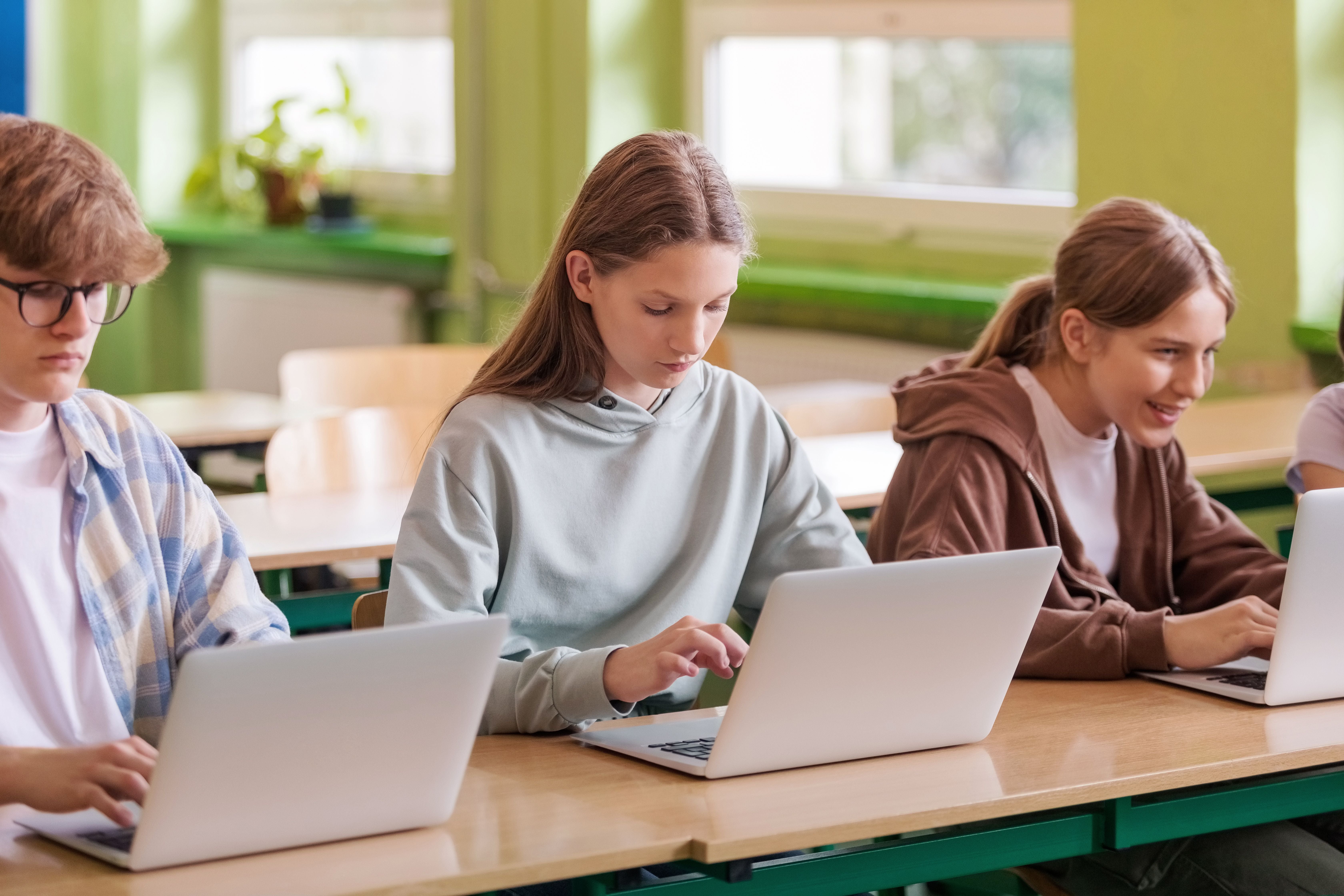 Drei Schüler arbeiten im Klassenzimmer an Laptops an ihren Schreibtischen.