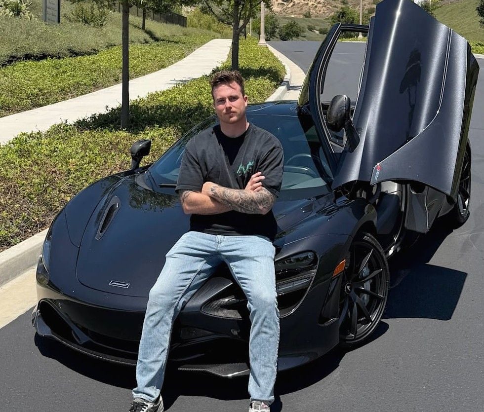 Ein Mann sitzt auf der Motorhaube eines schwarzen Sportwagens mit geöffneter Flügeltür.
