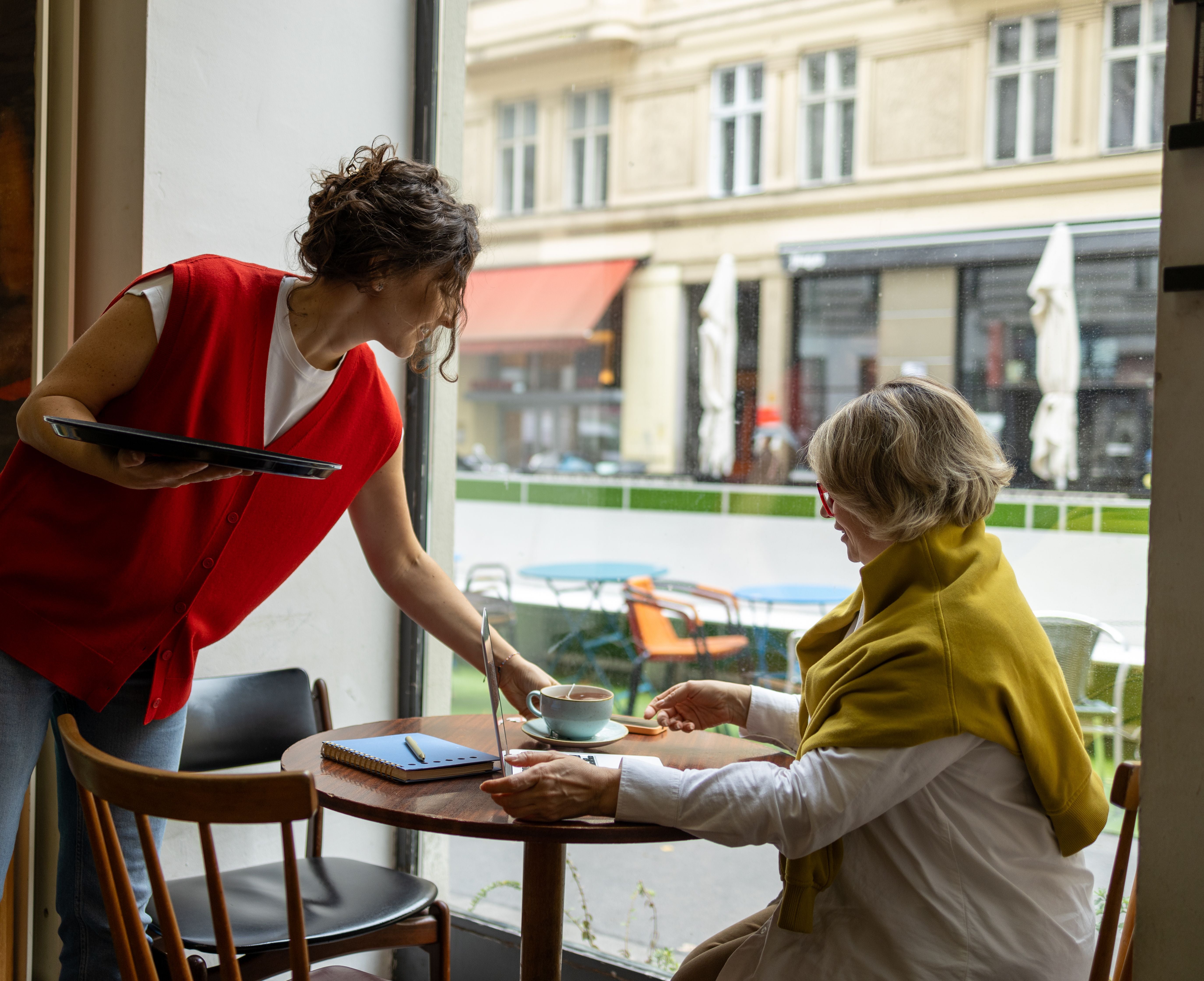 Kellnerin serviert einer Frau Kaffee an einem Tisch in einem modernen Café am Fenster.