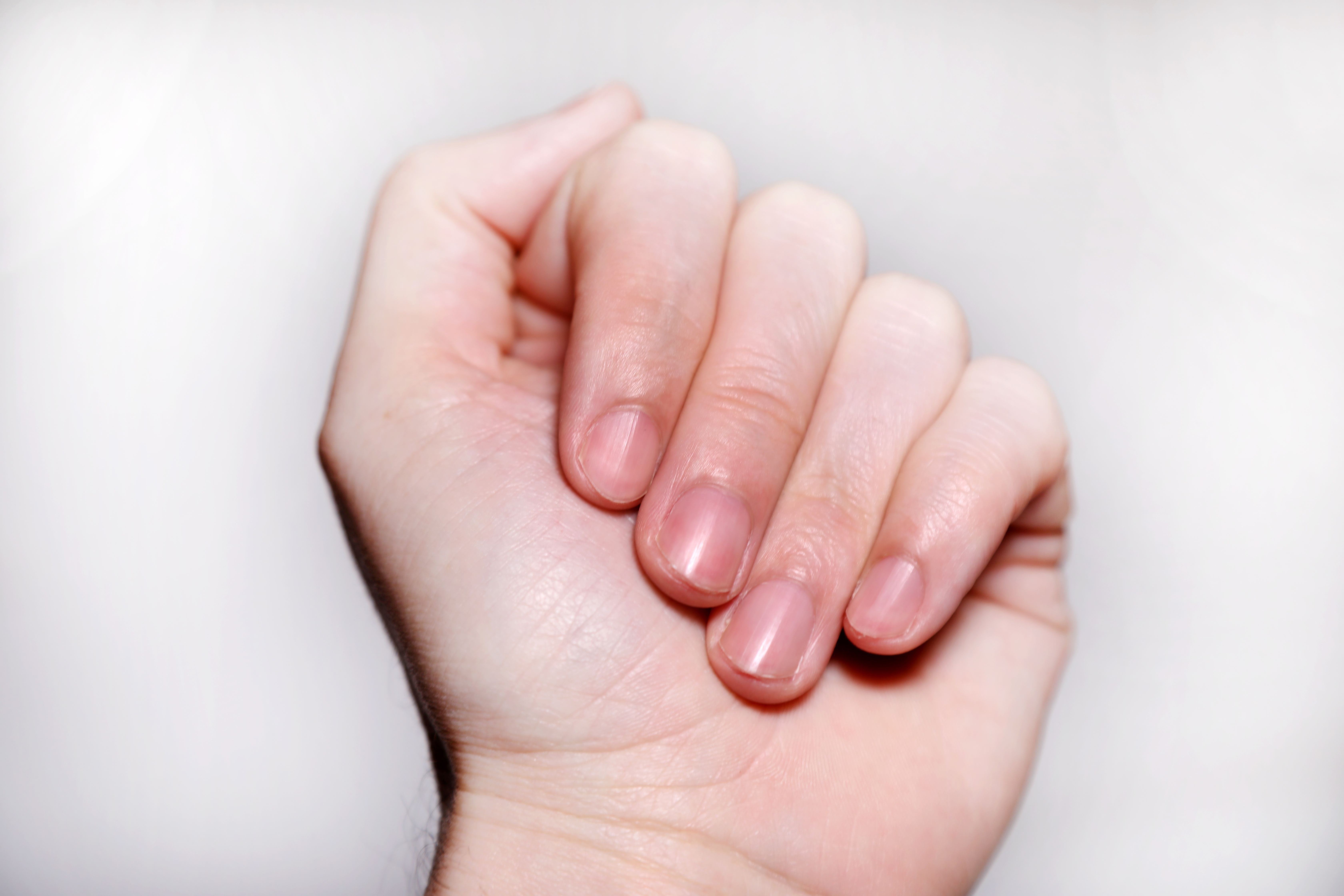 Nahaufnahme einer menschlichen Hand mit kurzen, sauberen Fingernägeln vor weißem Hintergrund.