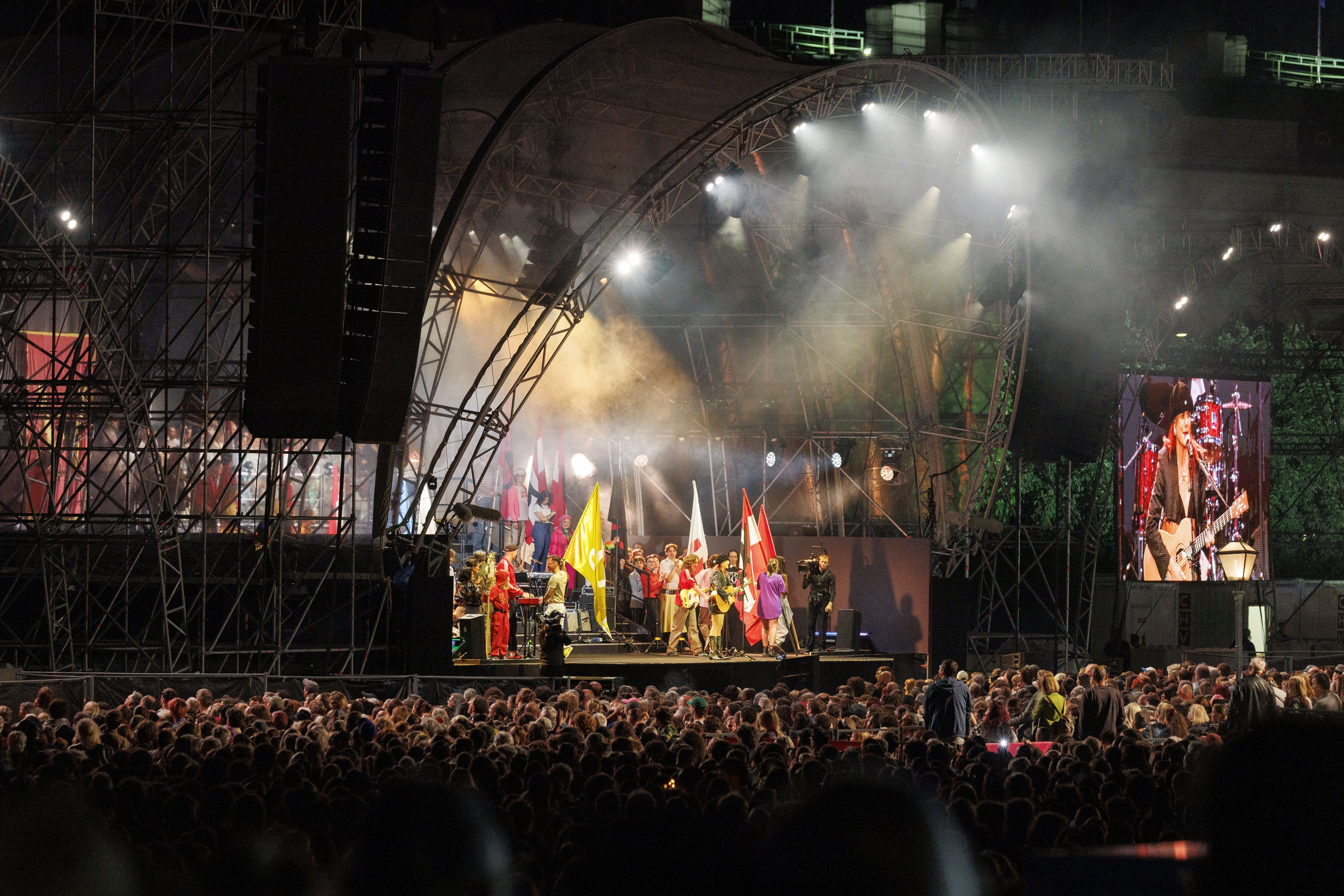 Bühne mit Musikern und Flaggen, große Menschenmenge beim Festwochen-Opening am Wiener Heldenplatz.