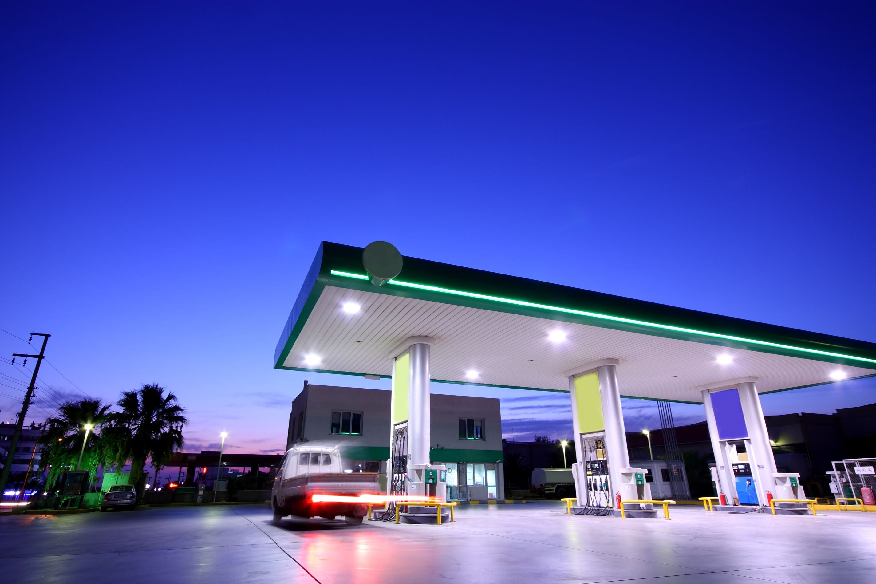 Beleuchtete Tankstelle bei Nacht mit einem Auto und klarem, blauem Himmel.