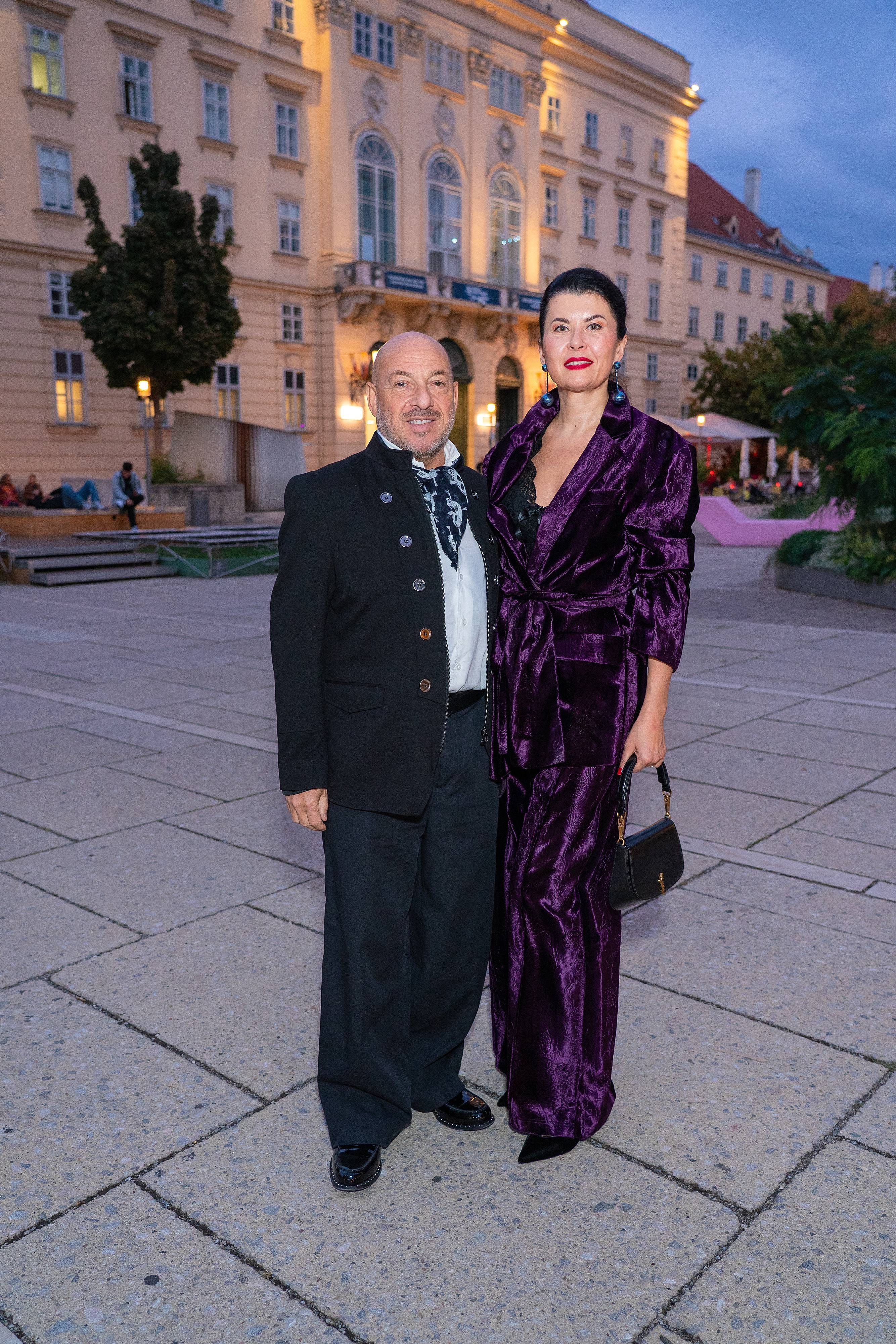 Ein Mann und eine Frau in eleganter Kleidung stehen vor einem historischen Gebäude.