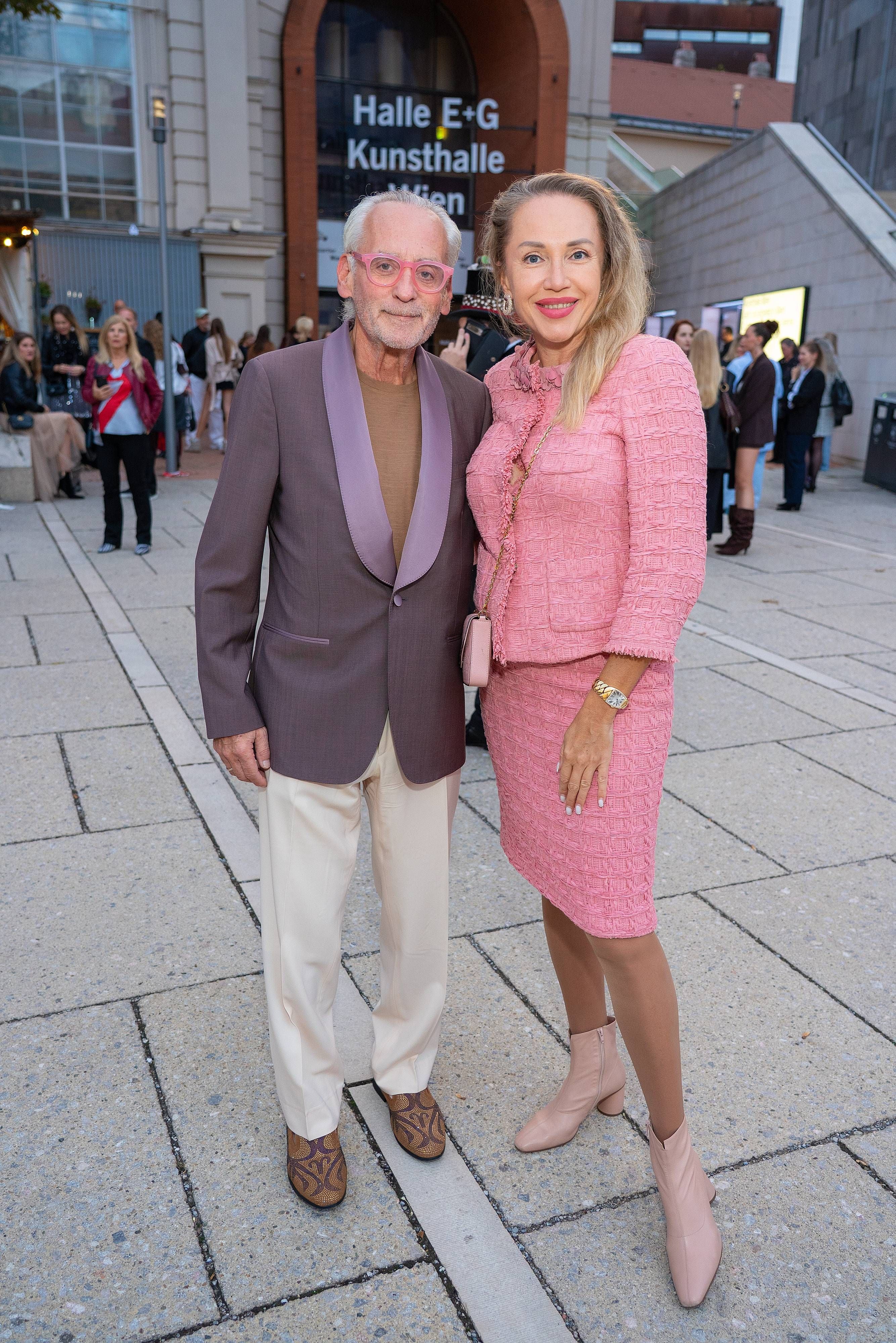 Ein Mann im Anzug und eine Frau im rosa Kostüm posieren vor der Kunsthalle Wien.