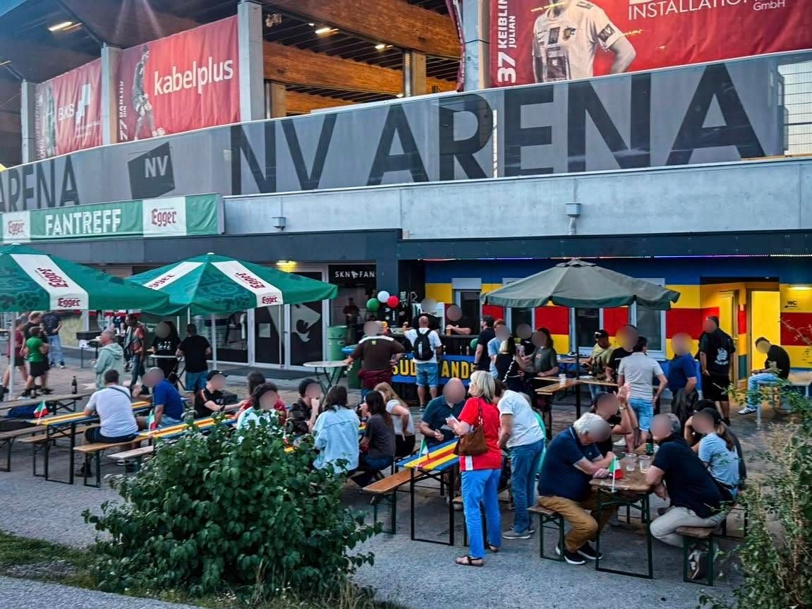 Menschen sitzen und stehen an Biertischen vor dem Eingang der NV Arena in St. Pölten.