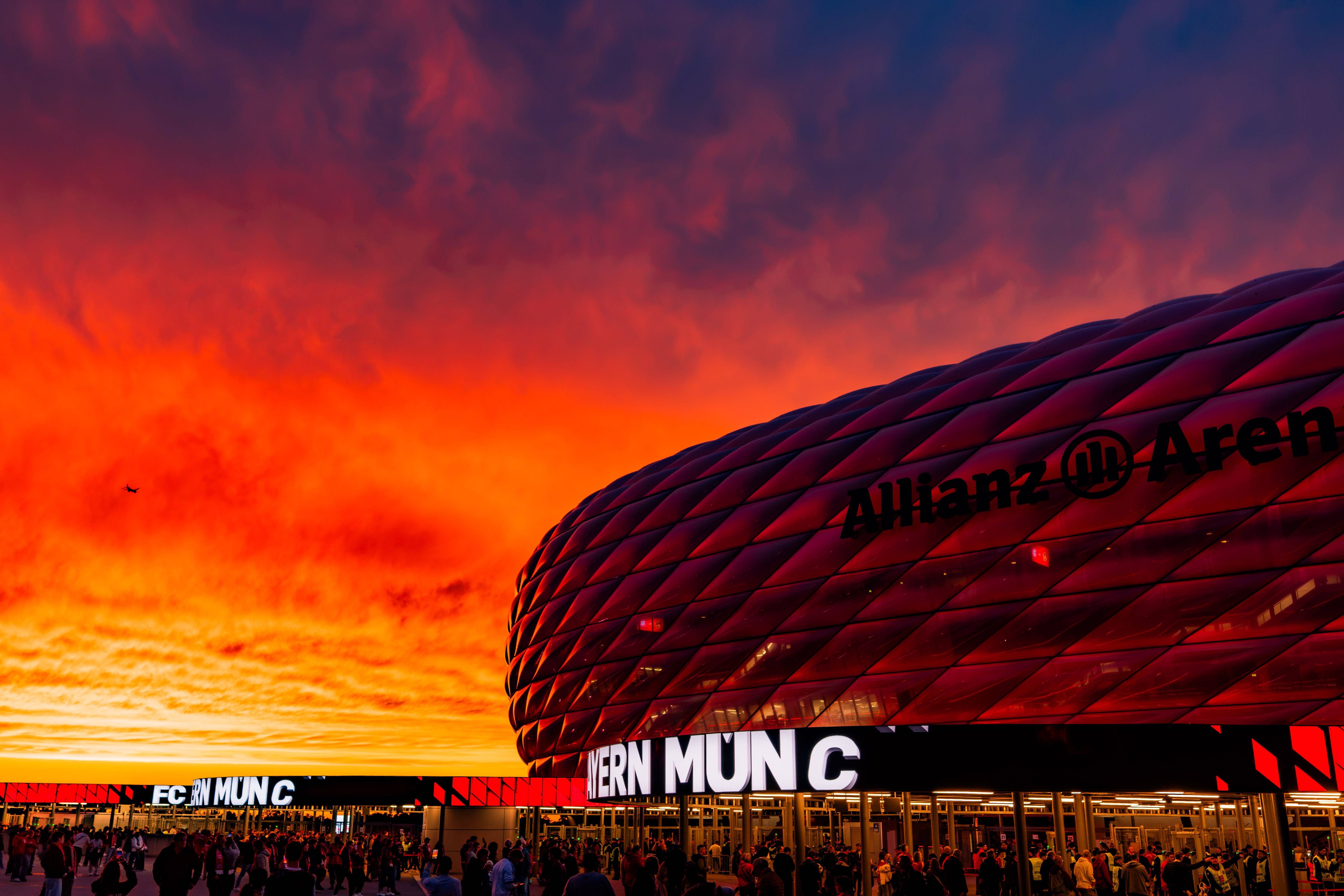 Die Allianz Arena bei Sonnenuntergang, Menschen strömen zum Champions-League-Spiel im Spätsommer.