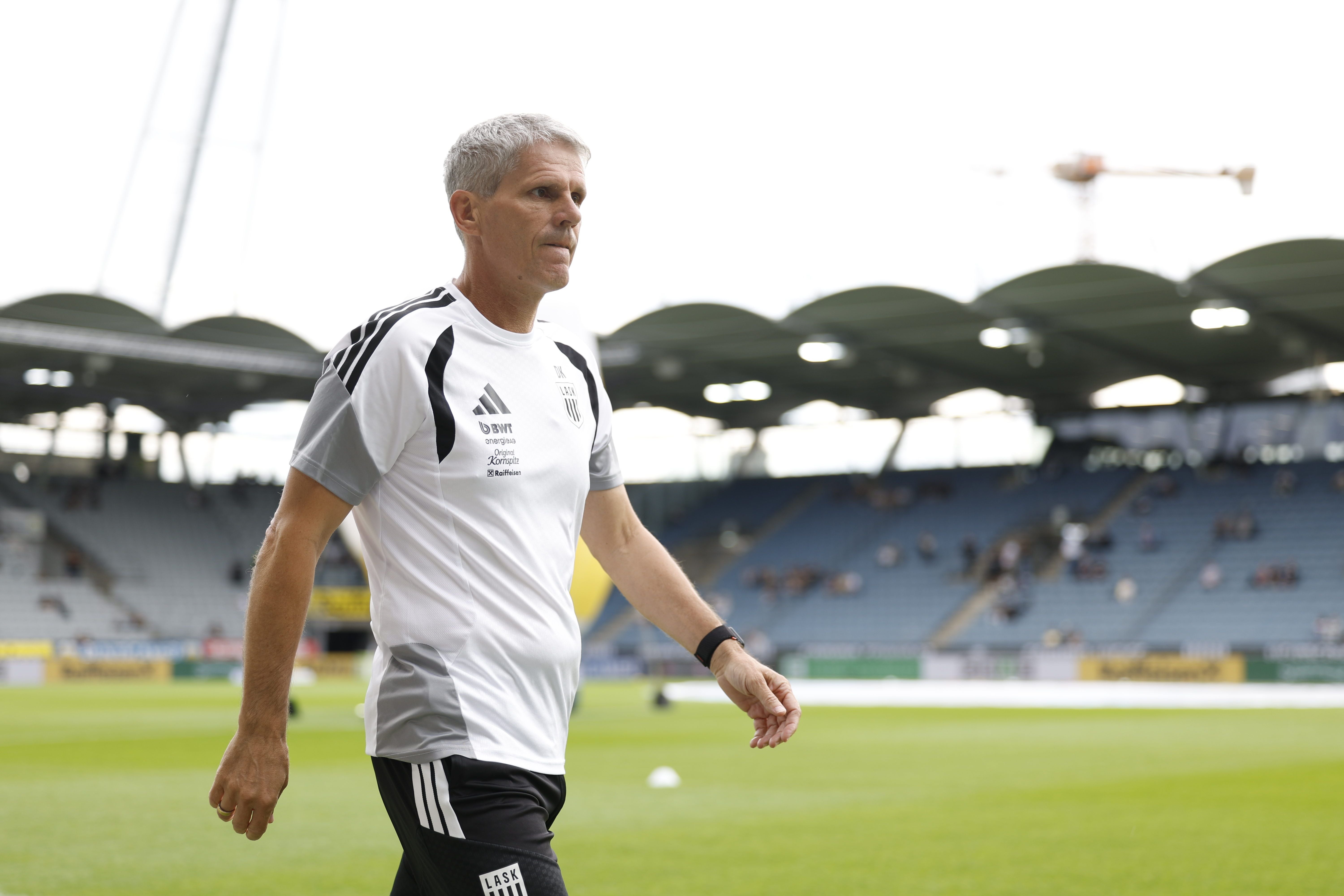 Ein Fußballtrainer im LASK-Trainingsanzug läuft am Spielfeldrand im Stadion.