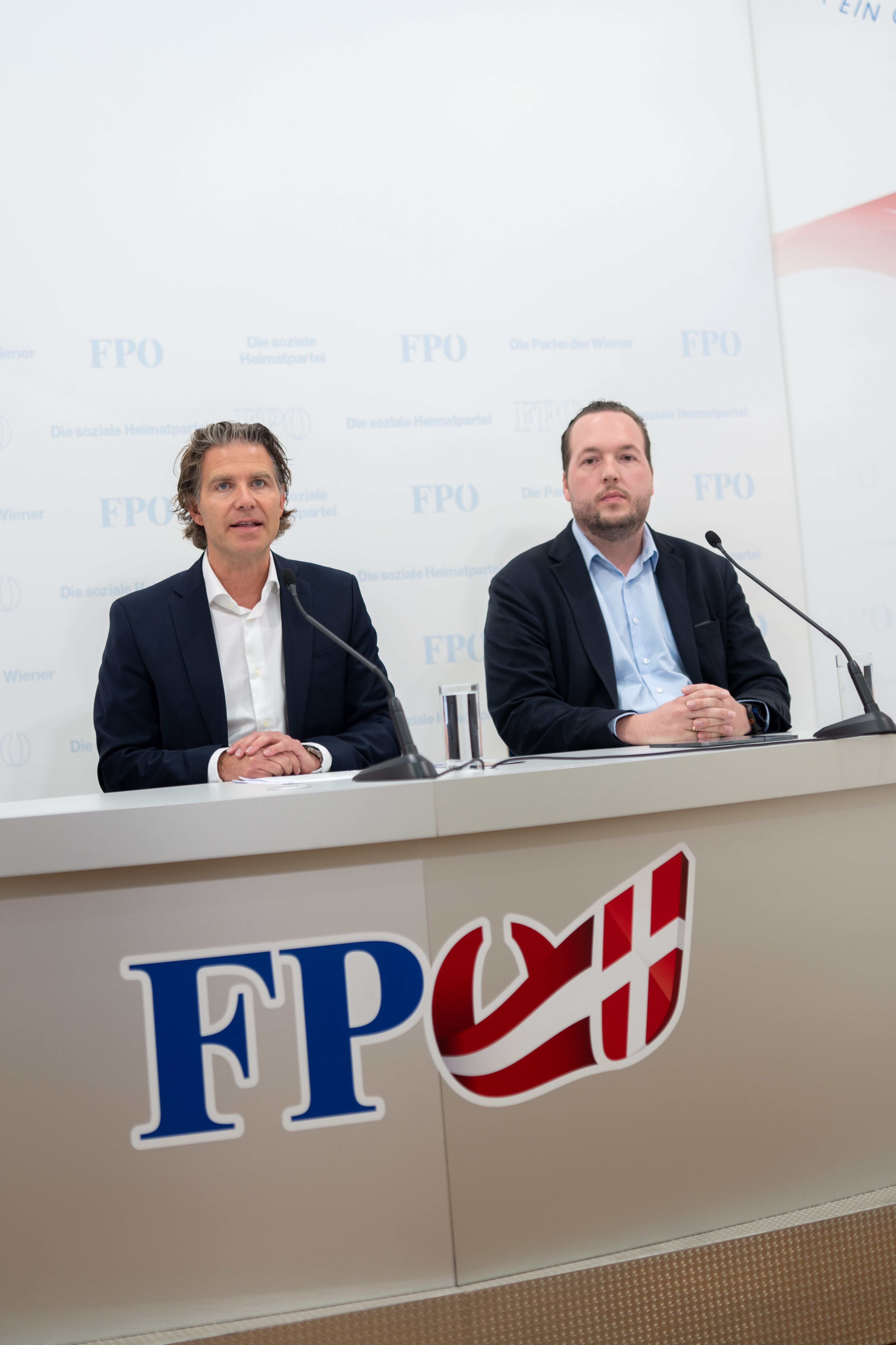 Zwei Männer sitzen bei einer Pressekonferenz der FPÖ hinter einem Tisch mit Mikrofons.